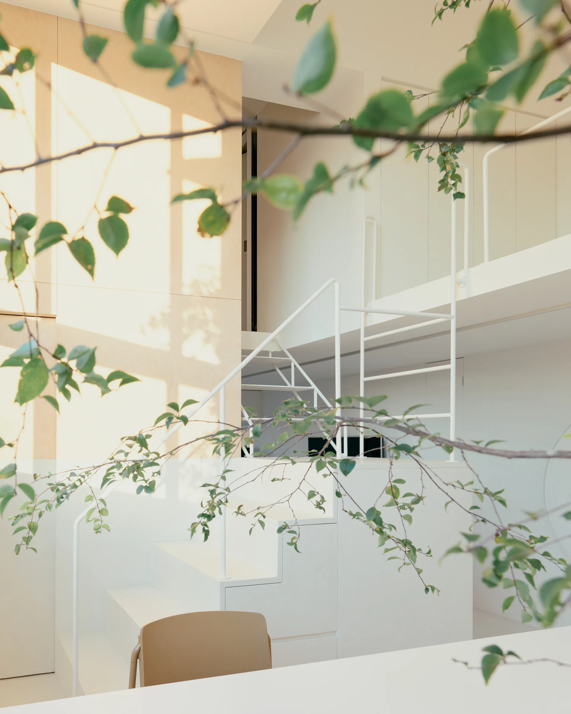 A minimalist white staircase with thin metal railings next to a light wood paneled wall leading to a mezzanine level.