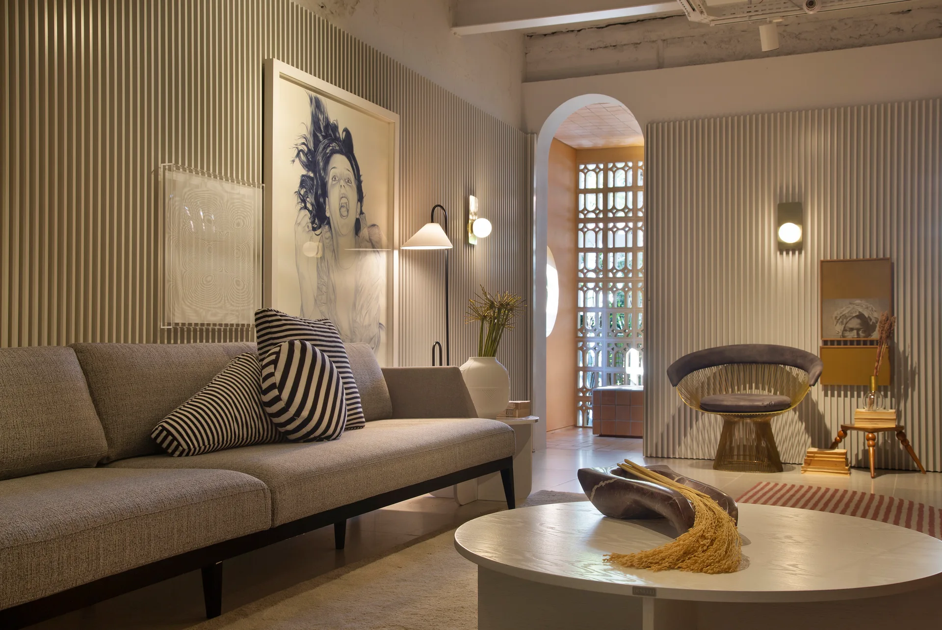A modern living room with a gray sofa, striped decorative pillows, a round coffee table, and walls covered in vertical fluted paneling.