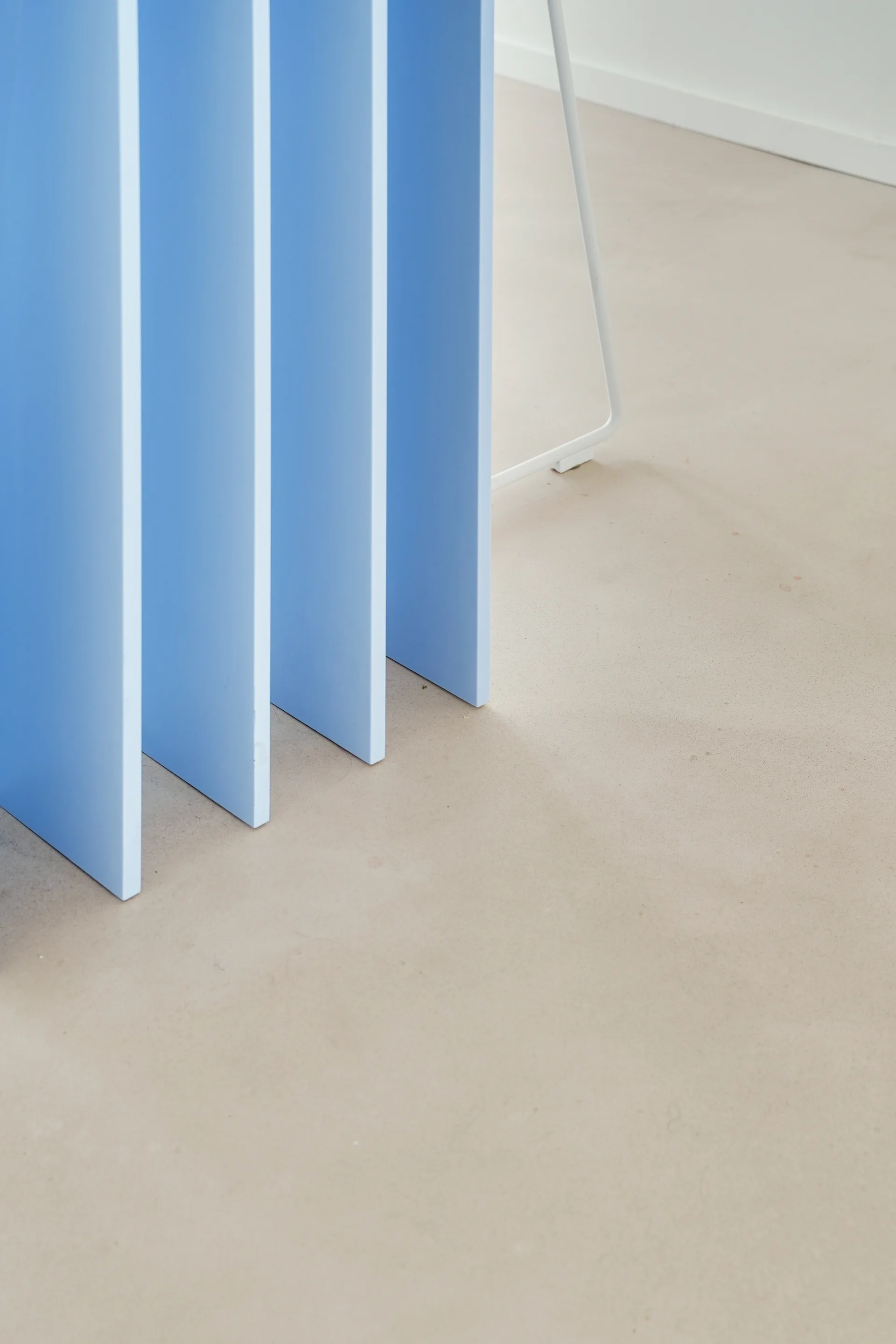 A series of vertical light blue partition fins stand on a smooth matte beige floor next to a white metal table leg.