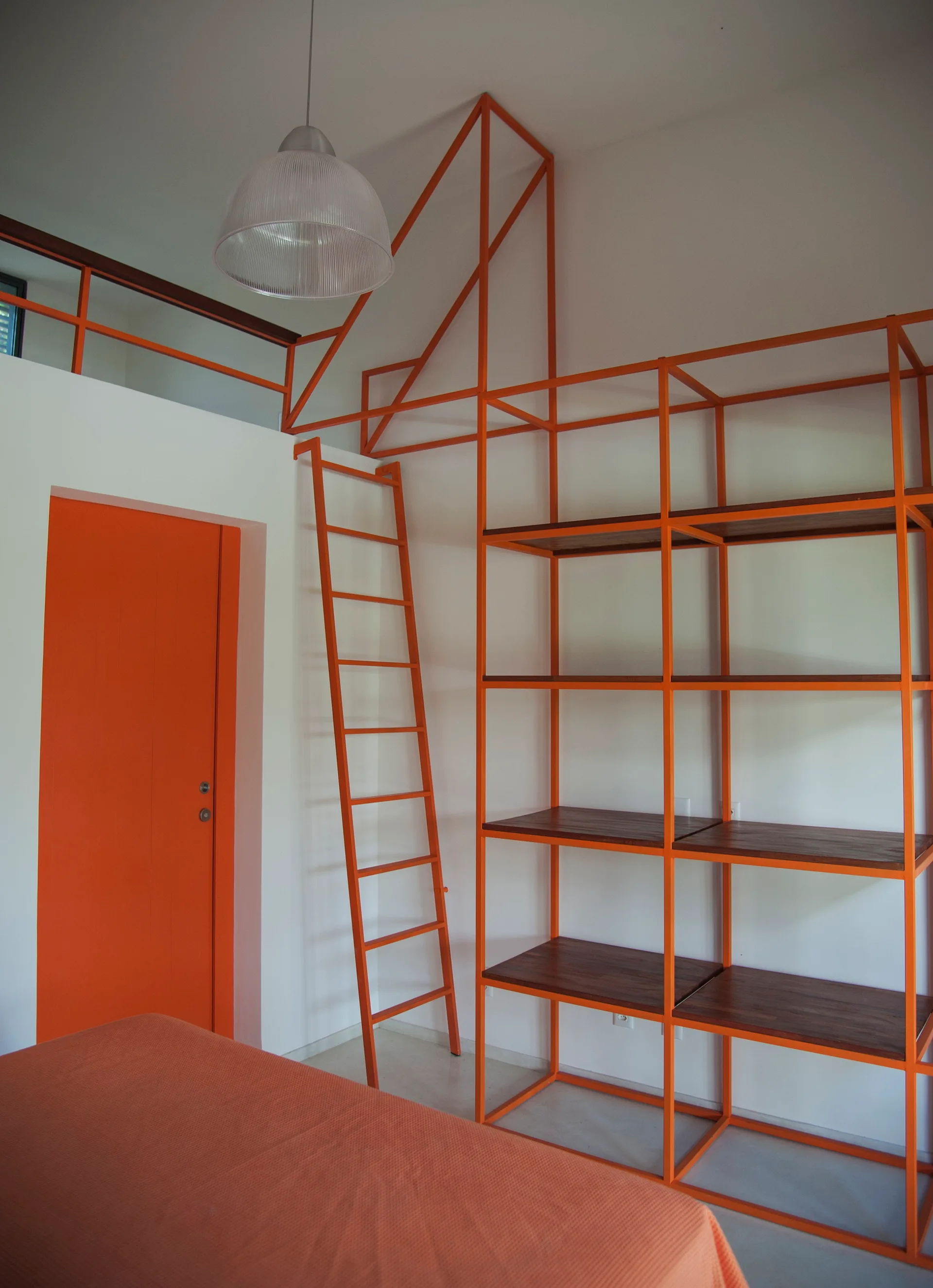 A modern white bedroom featuring a custom orange metal shelving unit and a matching orange ladder leading up to a loft mezzanine.