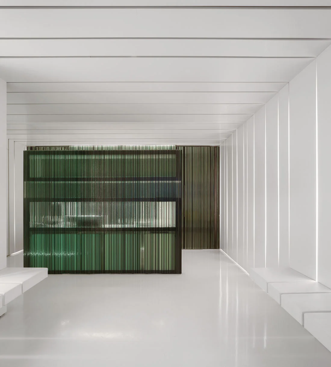 A minimalist white room features sleek built-in benches, linear wall paneling, and a green slatted room divider.