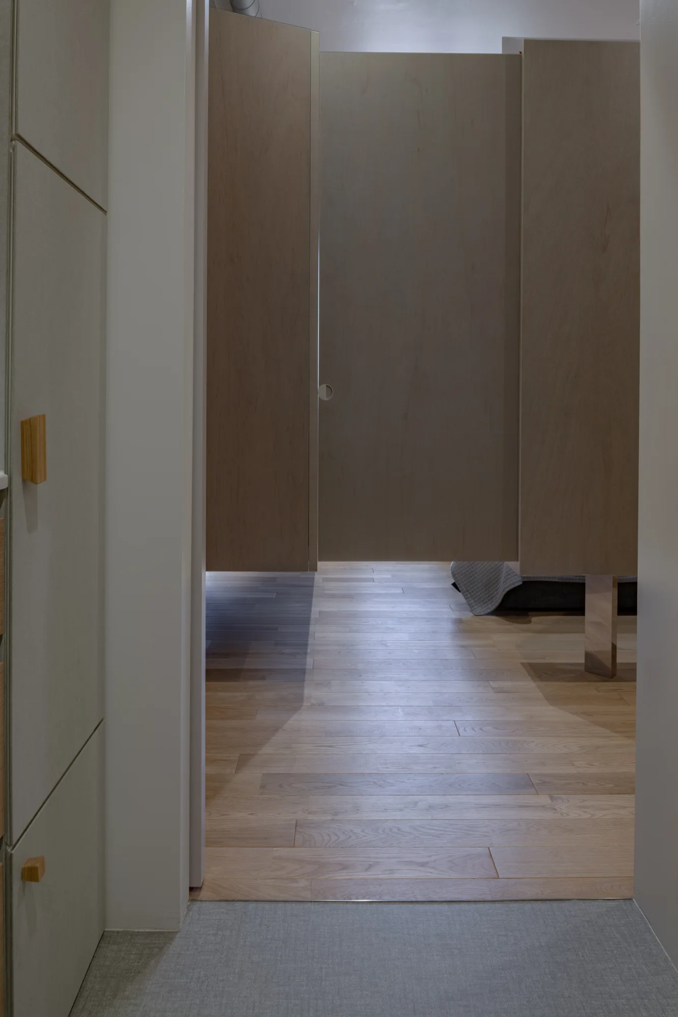 A view through a neutral doorway showing a floating wood partition wall and light wood flooring inside a bedroom.