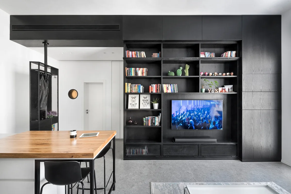 A modern living area with a large black floor-to-ceiling media unit, an integrated television, and a wood-topped counter with bar stools.
