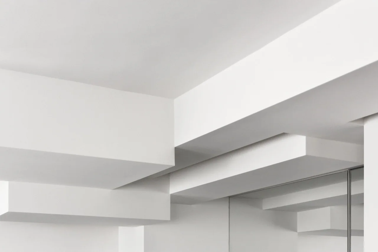 A close-up view of a minimalist interior showing layered rectangular ceiling beams painted in a uniform matte white finish.