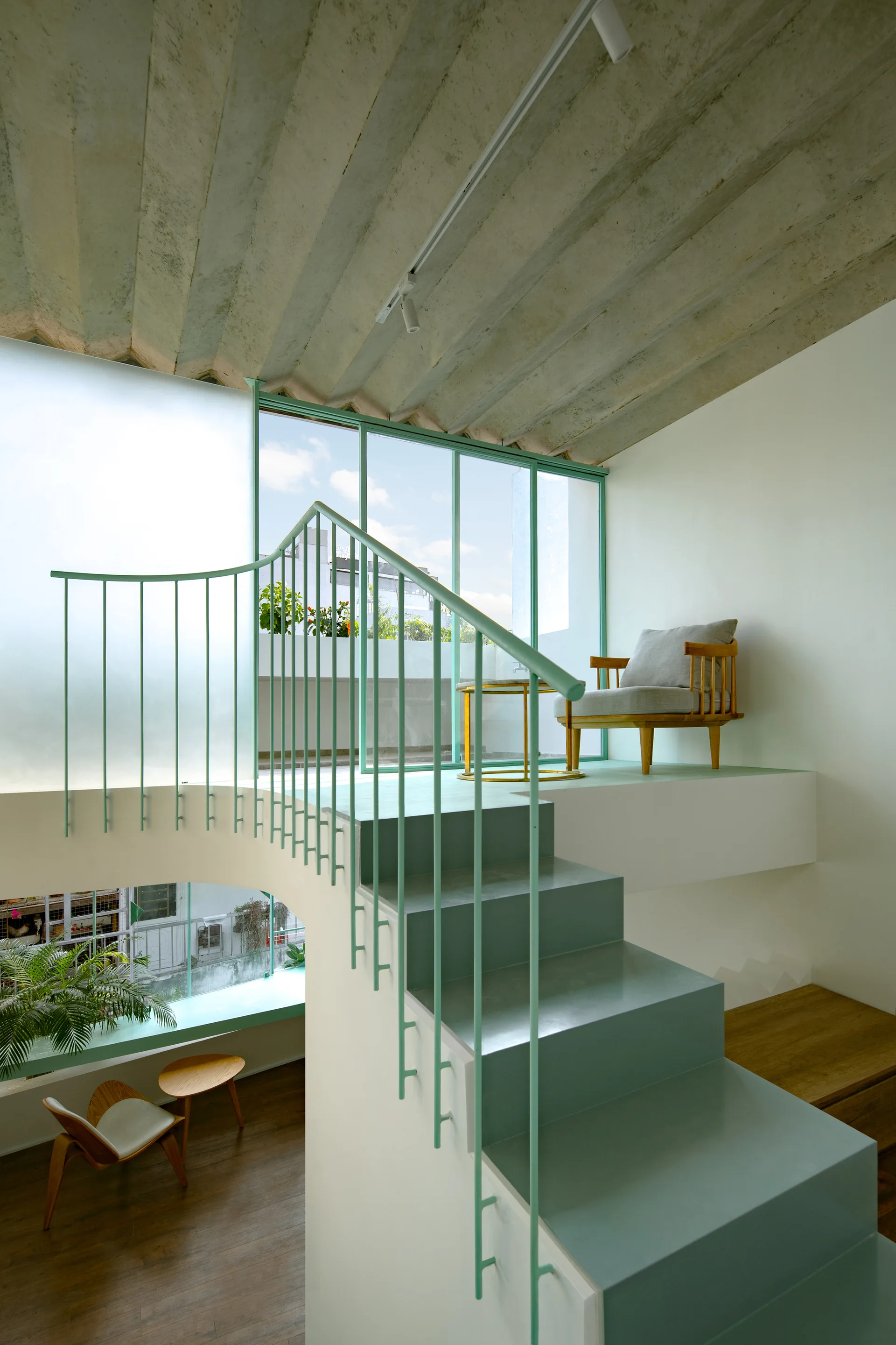A modern loft interior features a mint green staircase leading to a landing with a wooden armchair, set under a textured ribbed concrete ceiling.