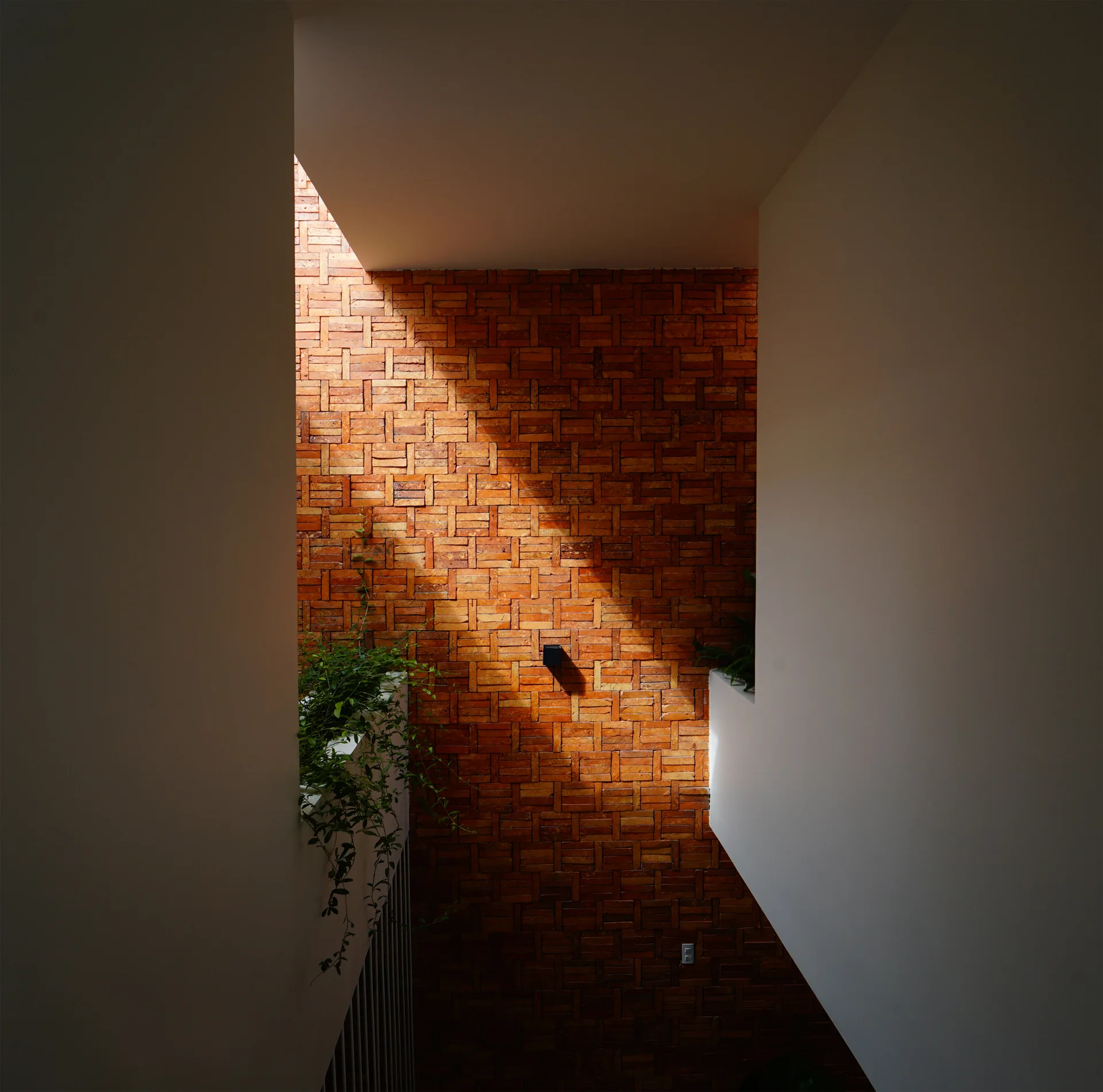 A modern white stairwell features a textured red brick accent wall illuminated by a dramatic beam of natural sunlight.