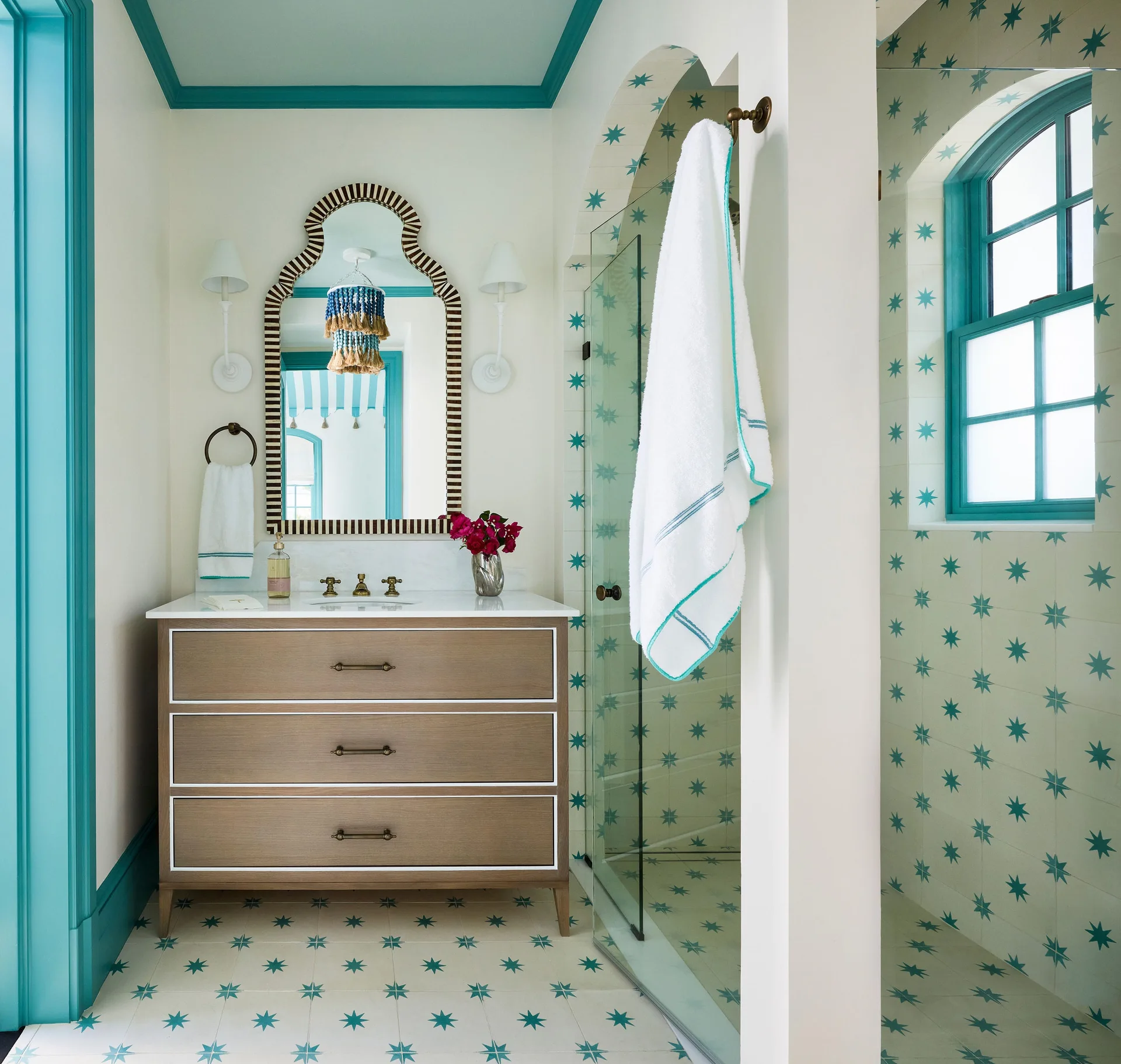 A Mediterranean style bathroom features a wood vanity, an arched striped mirror, and turquoise star-patterned tiles on the floor and shower walls.