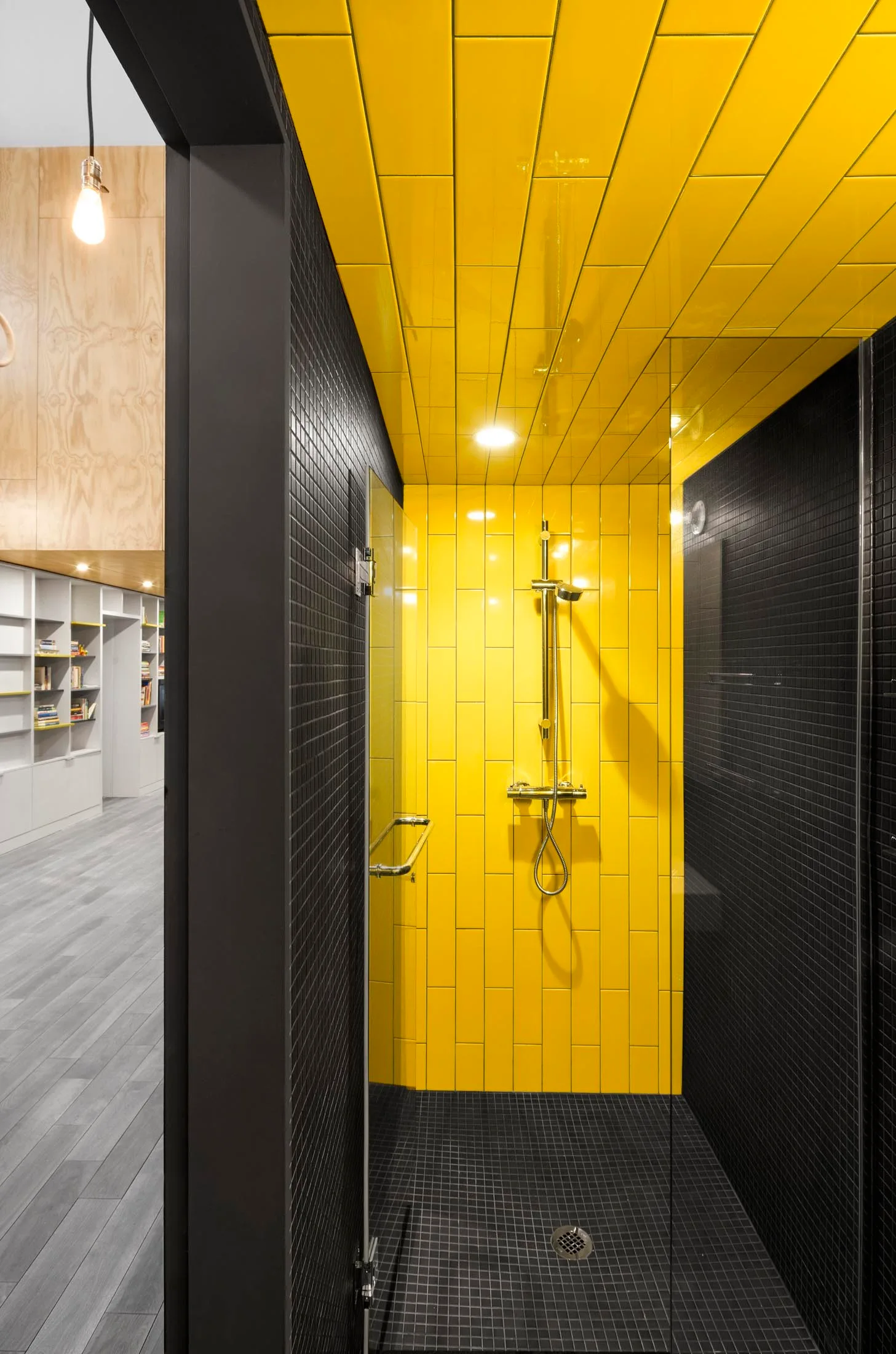 A modern walk-in shower with yellow subway tiles on the back wall and ceiling, black mosaic wall and floor tiles, and a gold shower head.