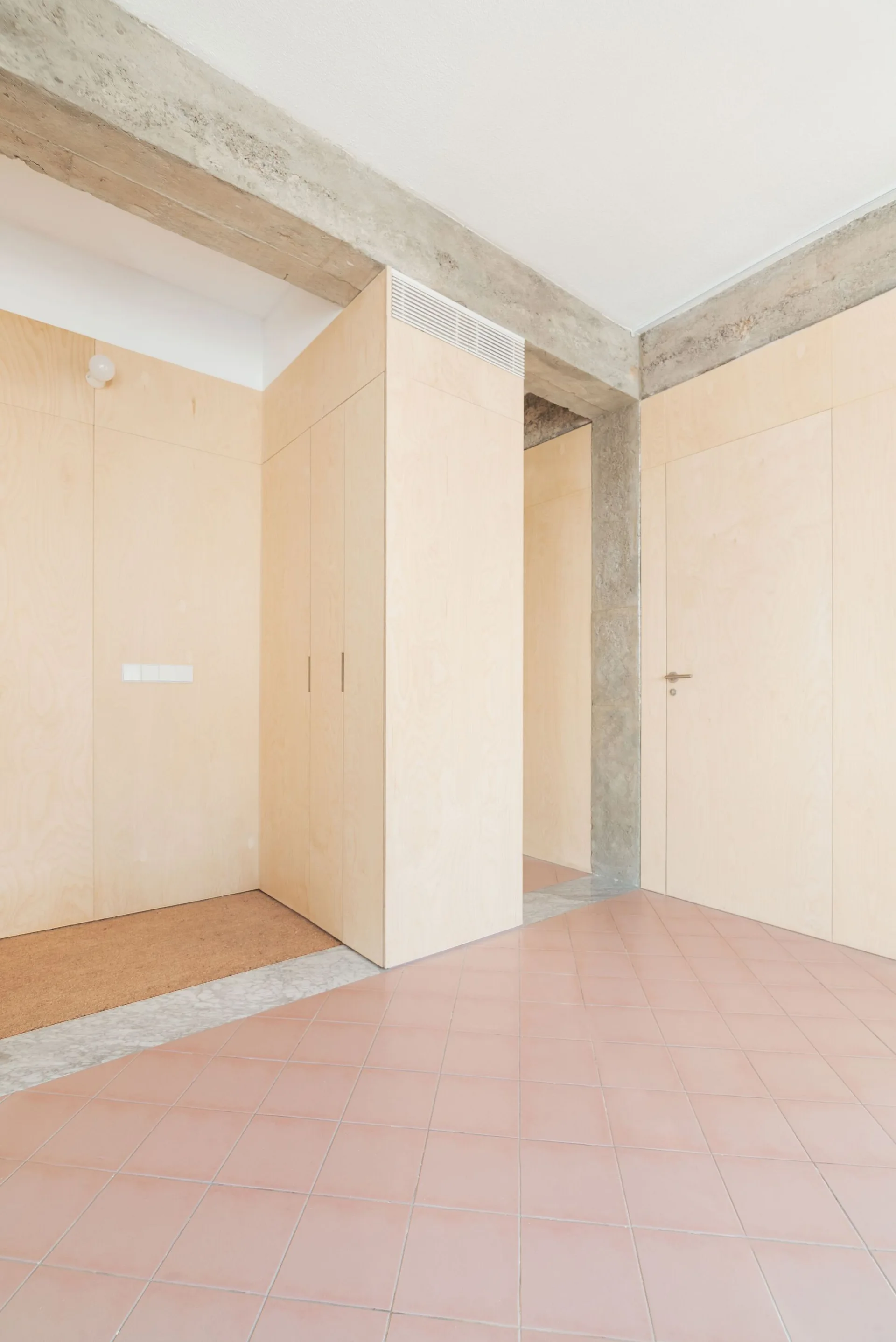 A modern minimalist entryway features light plywood wall paneling, pink tiled flooring, and exposed concrete structural beams.