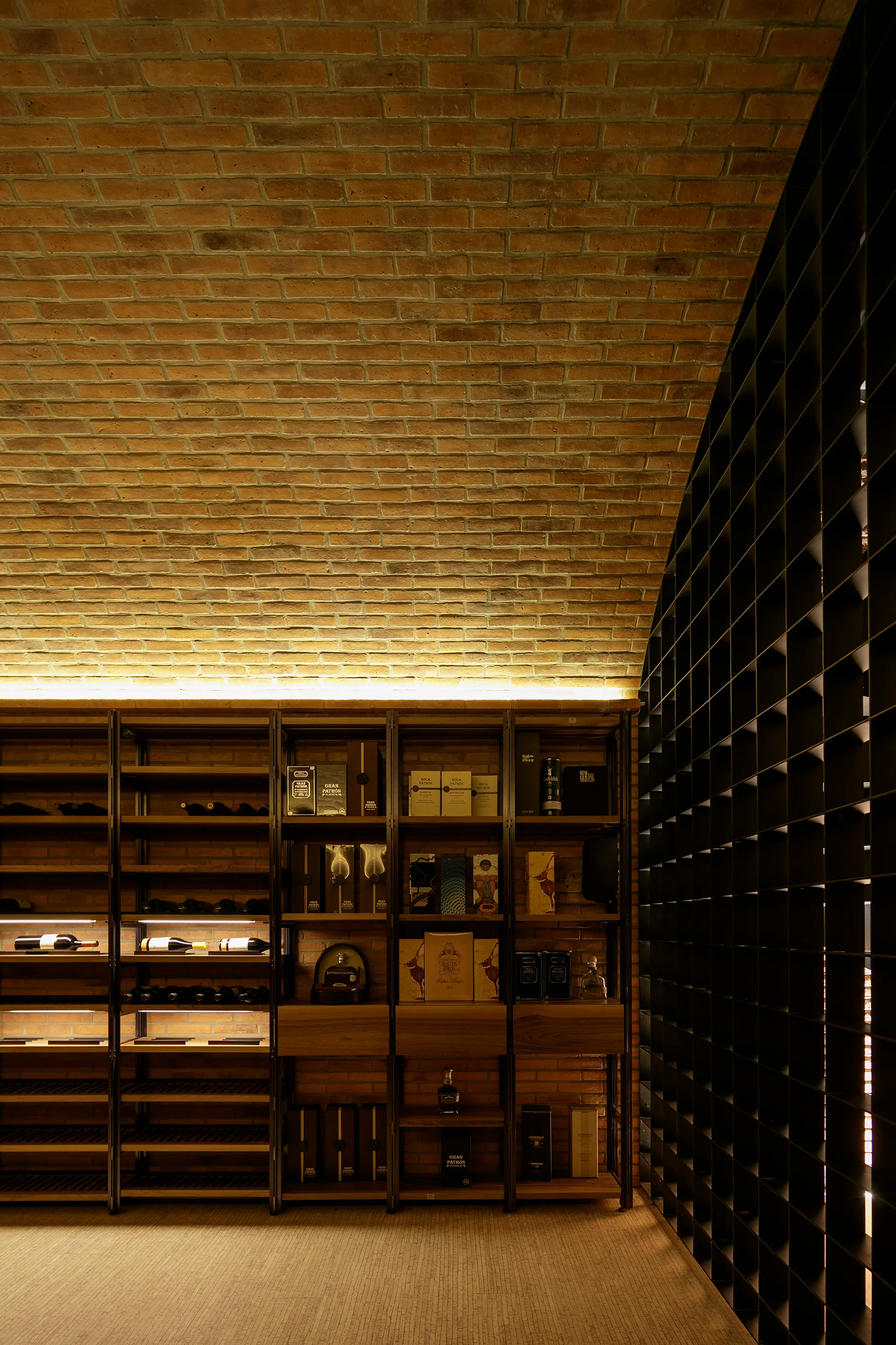 A modern wine cellar featuring a curved vaulted brick ceiling, built-in metal shelving with warm backlighting, and a dark grid partition.