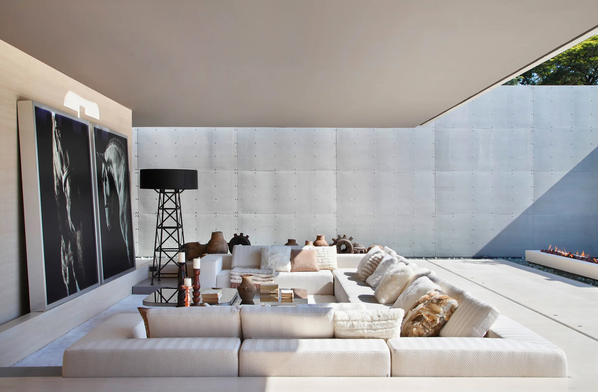 A large cream sectional sofa with textured pillows sits on a concrete patio next to large black-and-white artwork and a concrete wall.