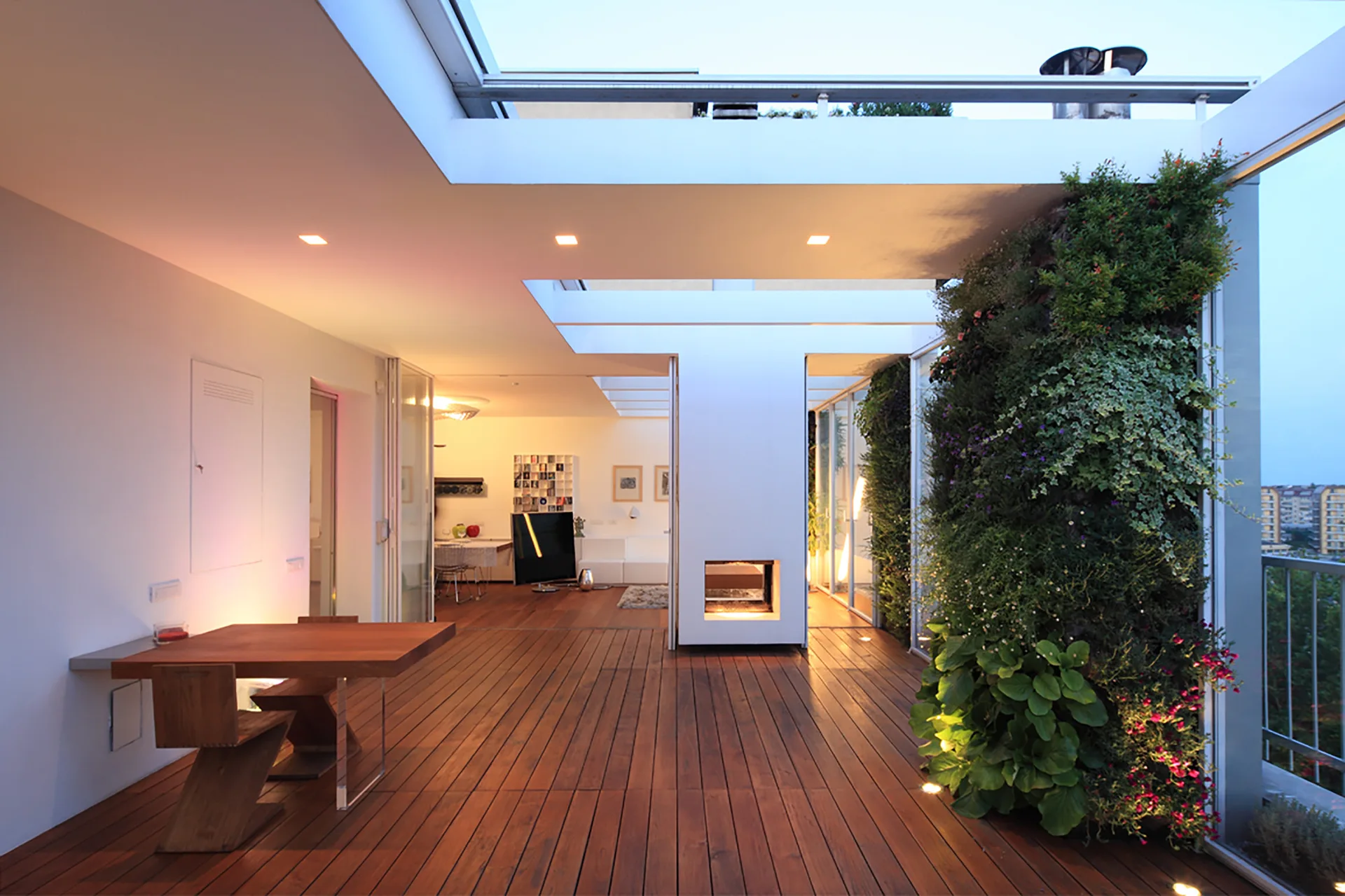 A modern outdoor terrace features dark wood plank flooring, a lush green vertical garden wall, and an integrated fireplace pillar.