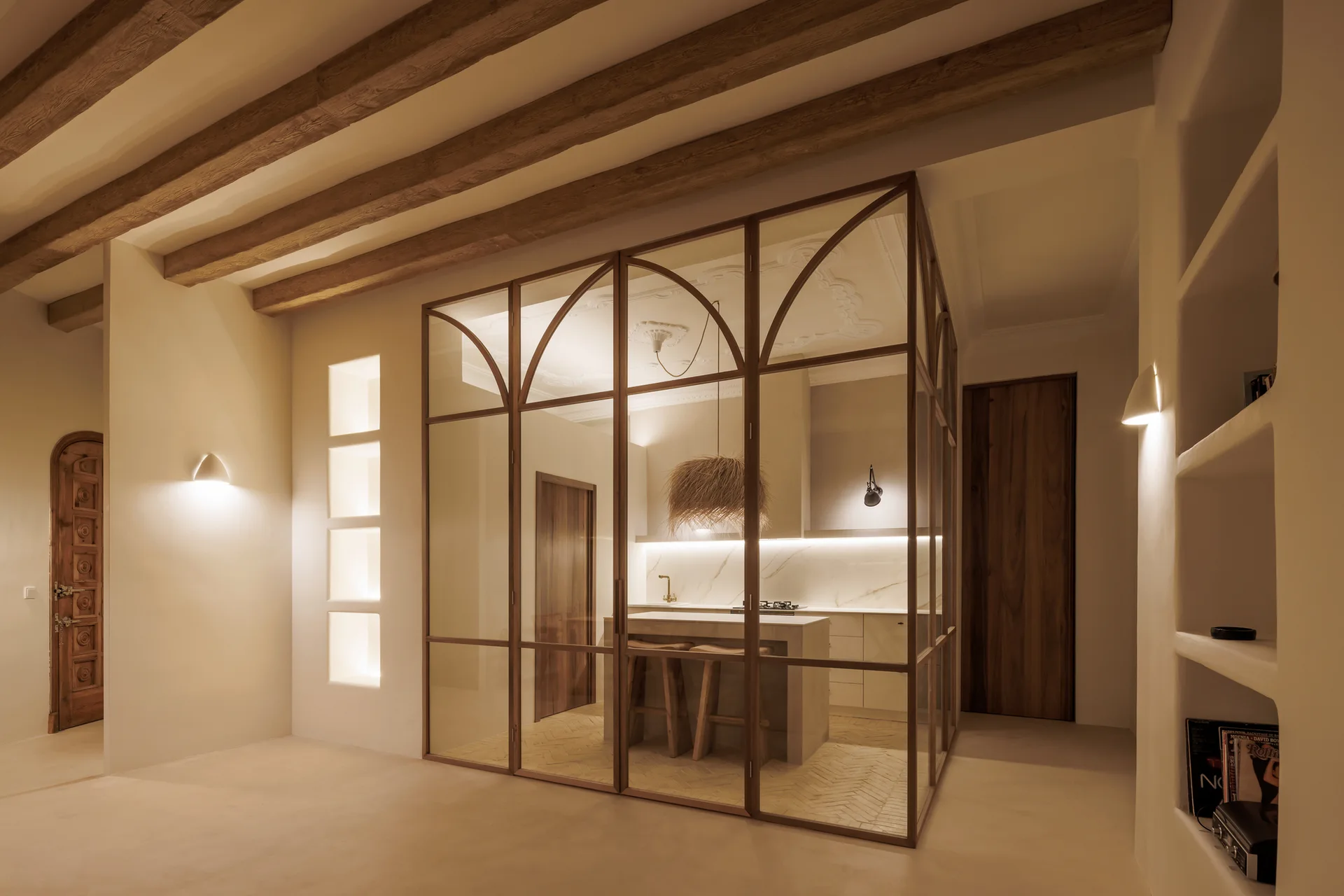 A kitchen enclosed by a metal and glass partition with arched panels under a ceiling with exposed wooden beams.
