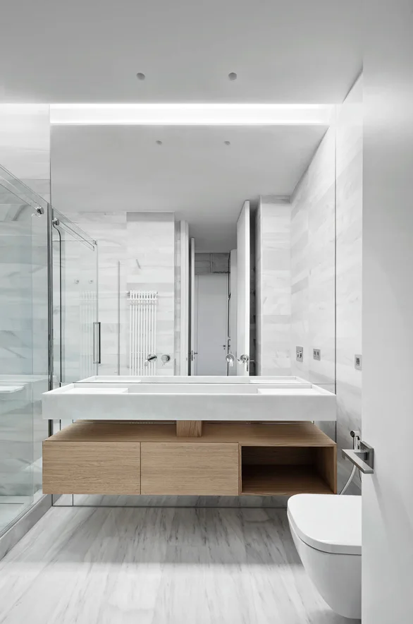 A modern bathroom features a floating wood vanity with an integrated white sink, veined marble tiled walls and floor, and a large mirror.