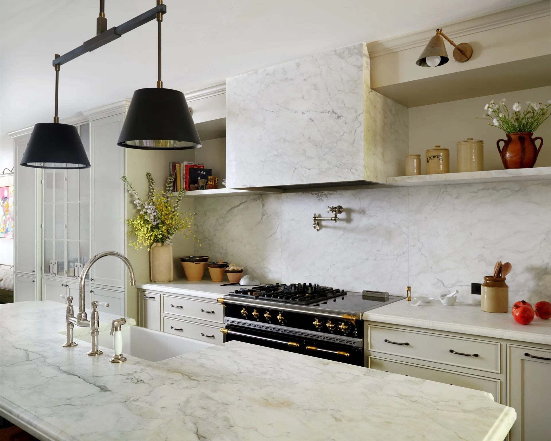 A cream kitchen featuring a white veined marble backsplash, matching marble-clad range hood, black stove, and marble-topped island.