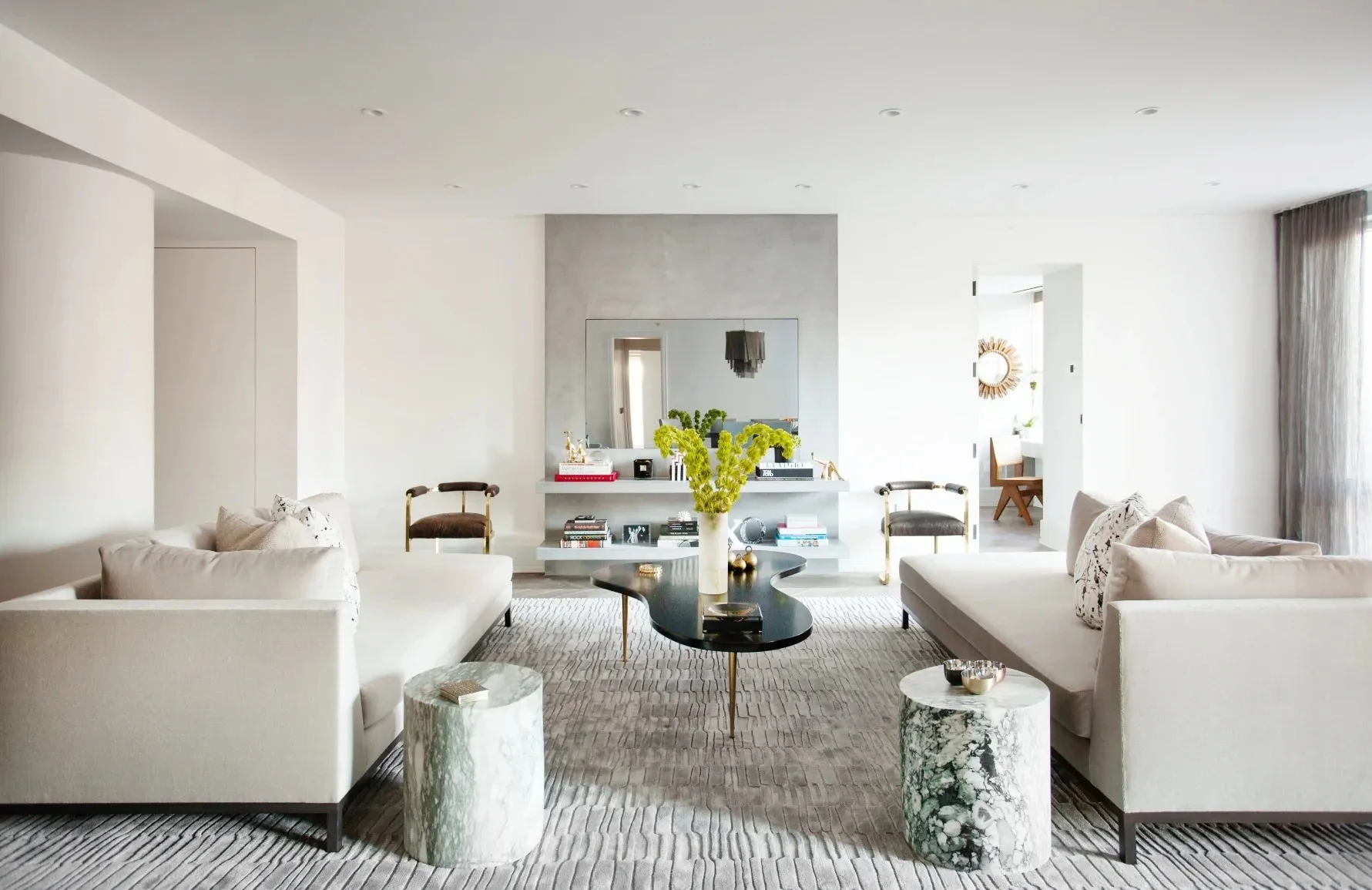 Two cream sofas face each other across an organic black coffee table on a textured gray rug with cylindrical marble side tables.