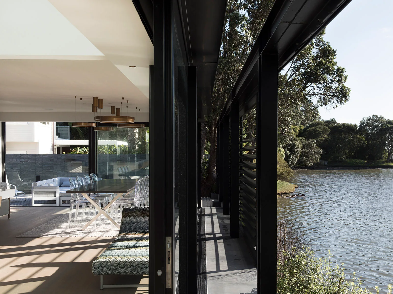 A modern dining room features clear acrylic chairs around a large table next to sliding glass doors that open to a waterfront deck.