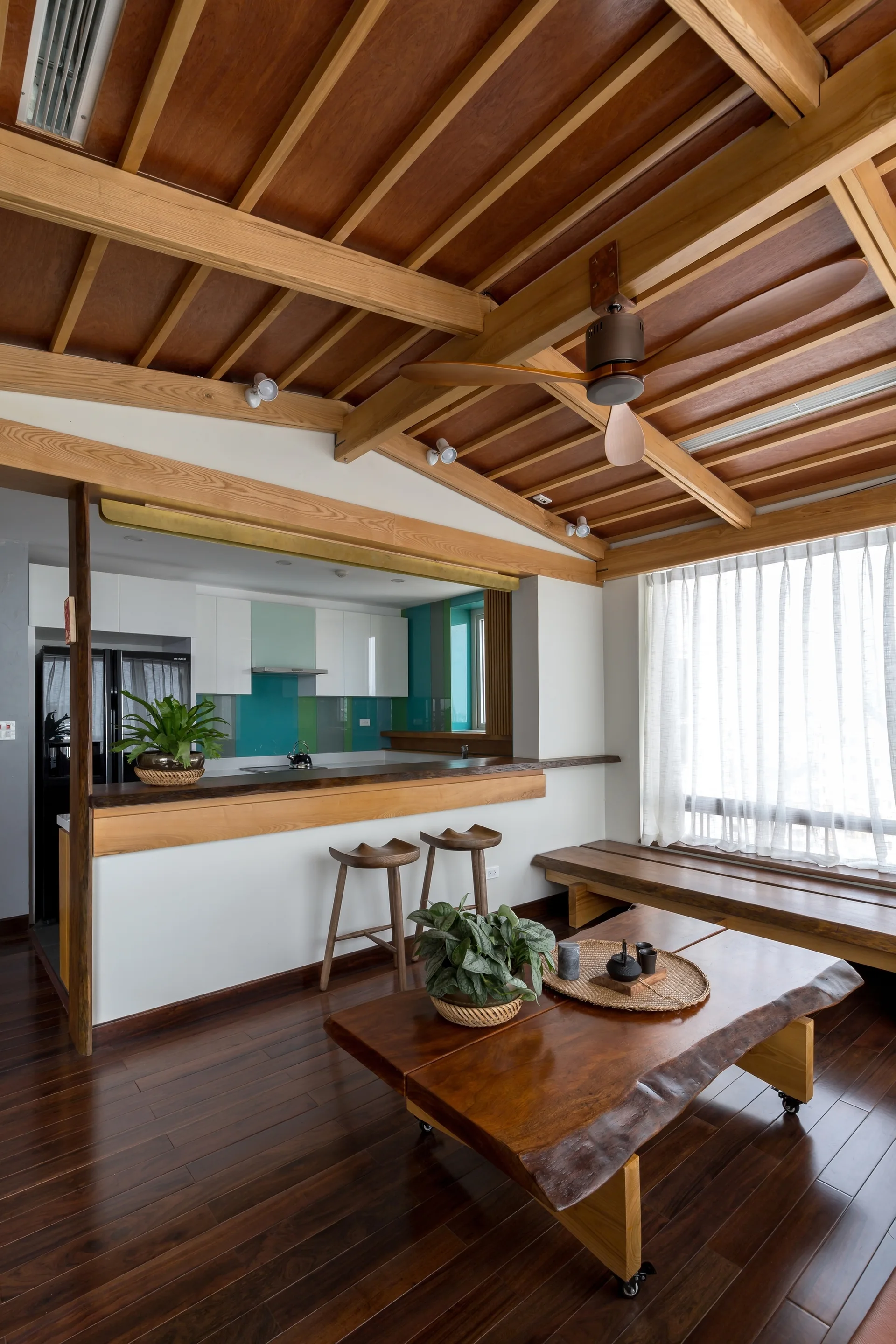 An open kitchen and living area with a vaulted wood beam ceiling, white cabinets, a teal backsplash, and a live-edge wooden coffee table.