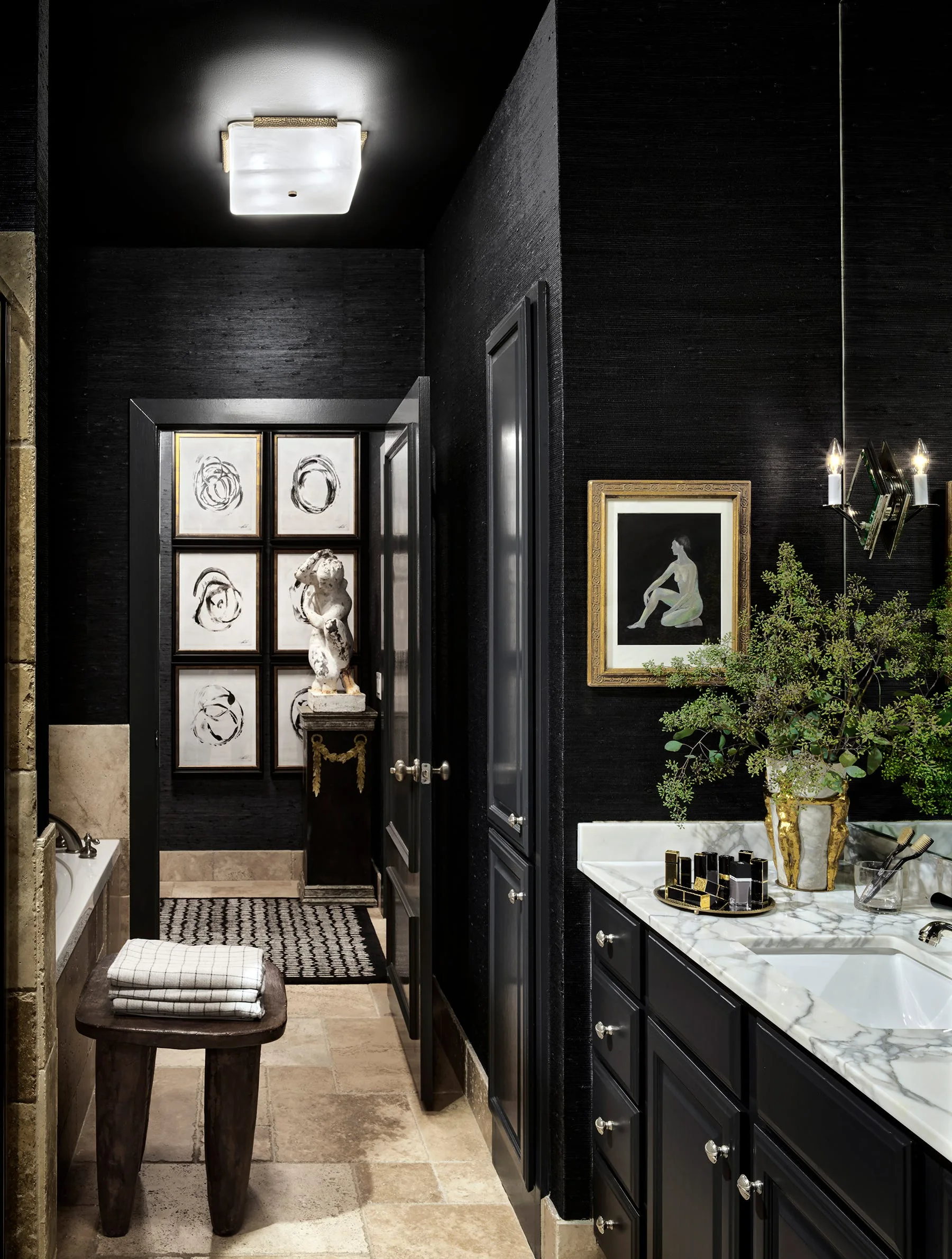A dark bathroom features black grasscloth walls, a black painted ceiling, a white marble vanity, and a wooden stool next to the bathtub.