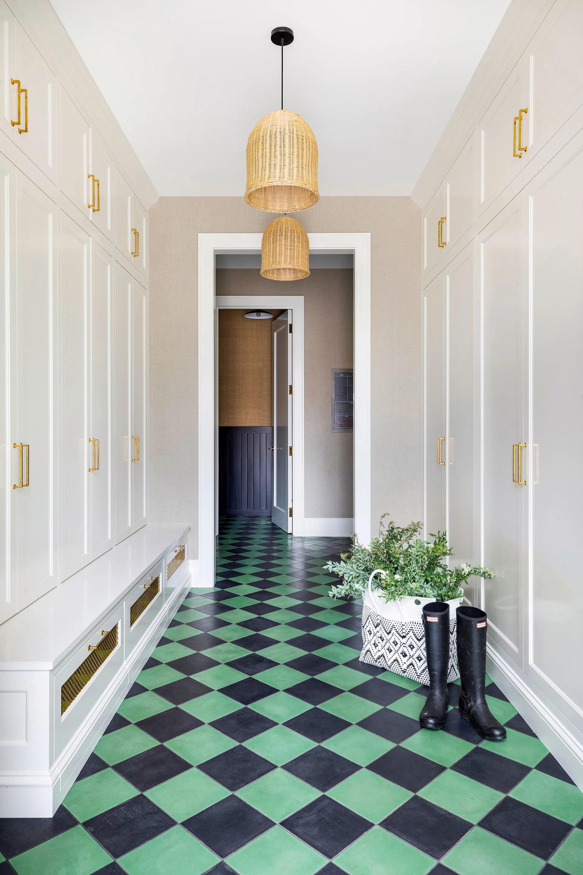 A symmetric mudroom featuring floor-to-ceiling white cabinetry with gold pulls, two woven pendant lights, and a green and black checkerboard tile floor.