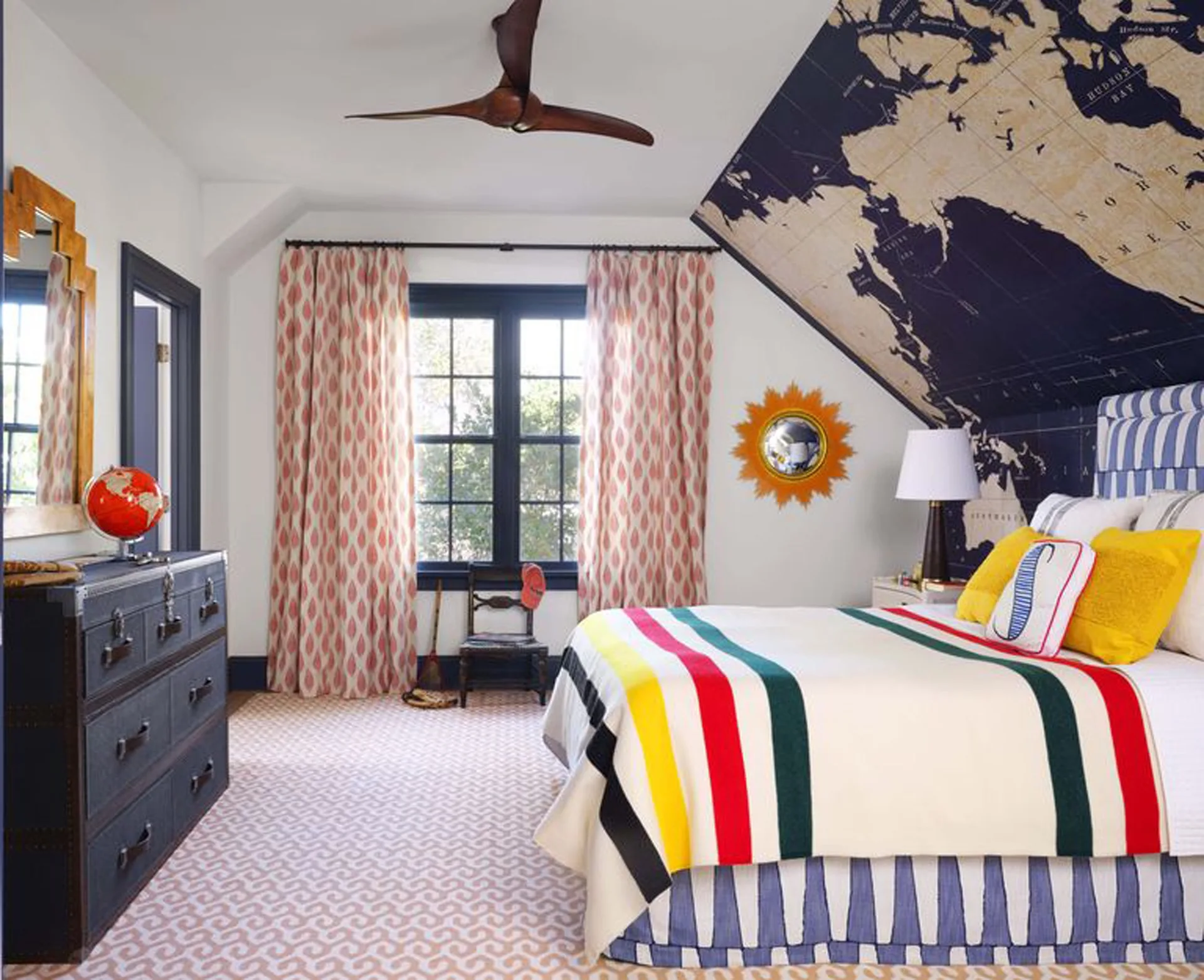 An attic bedroom features a world map mural on the sloped wall, a bed with a striped Hudson Bay blanket, and a trunk-style chest.