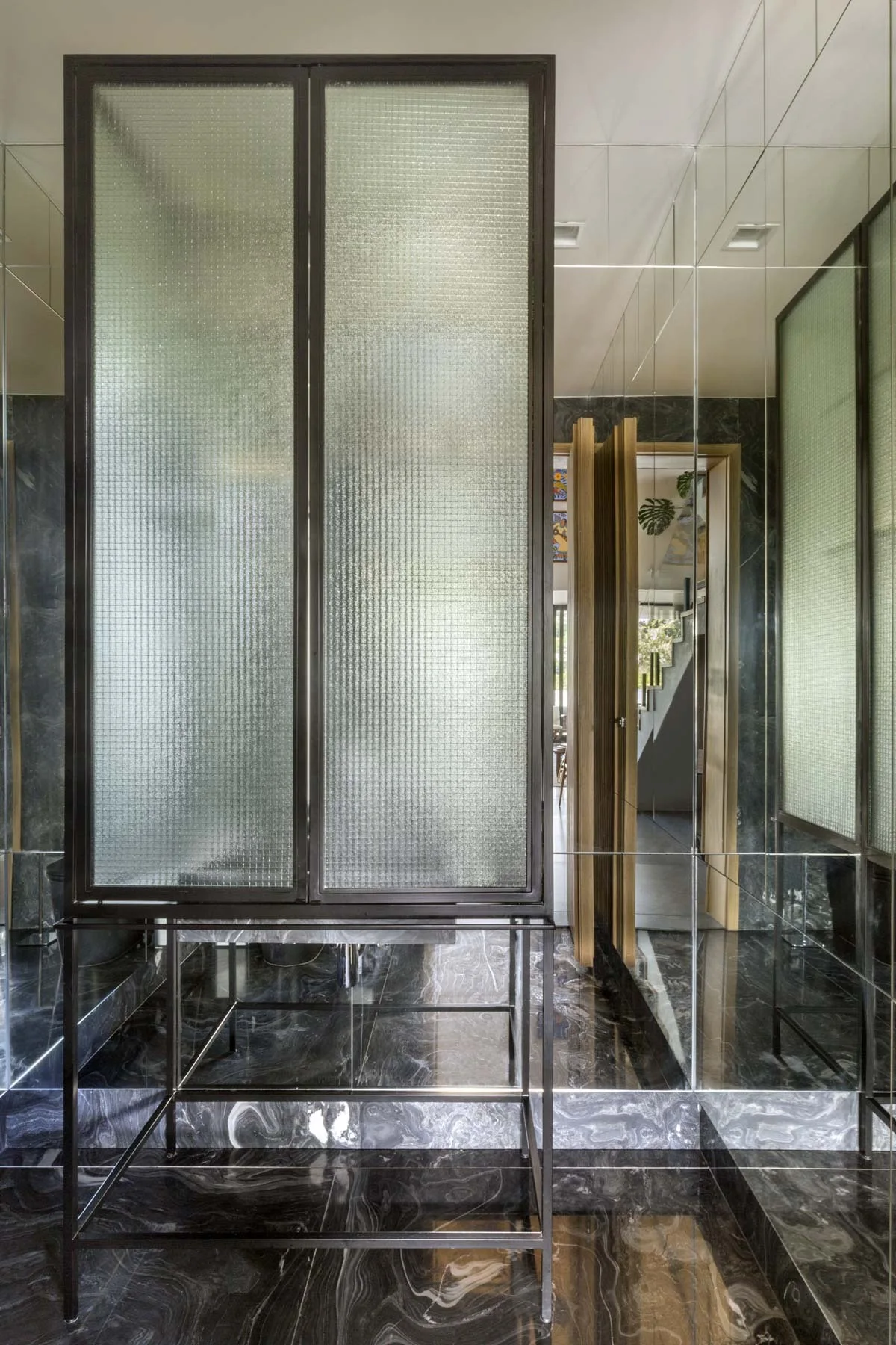 A tall textured glass screen framed in dark metal stands in a bathroom with polished black marble floors and mirrored walls.