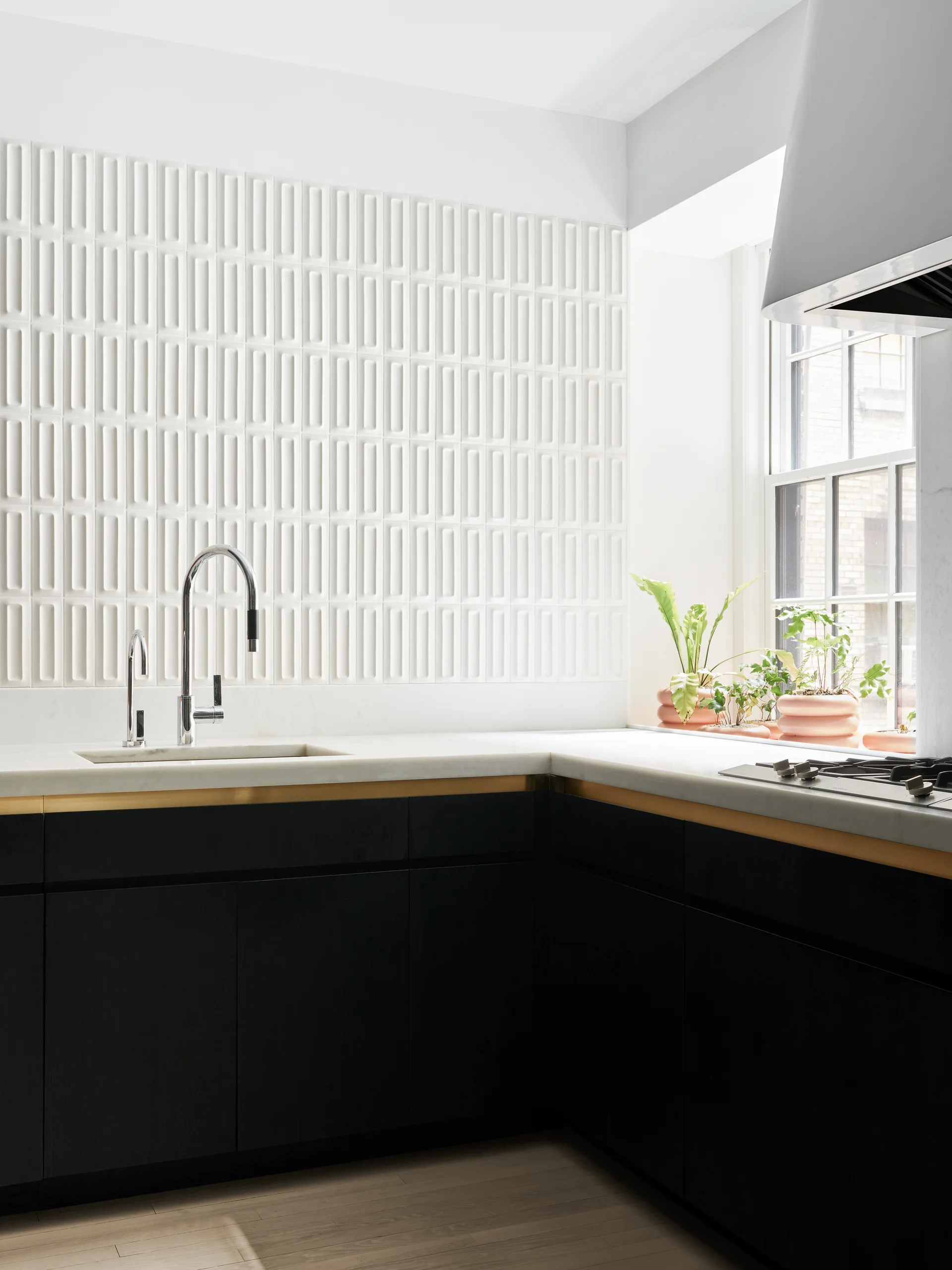 Matte black kitchen cabinets with a gold reveal strip, white marble countertops, a chrome faucet, and a textured white rectangular tile backsplash.