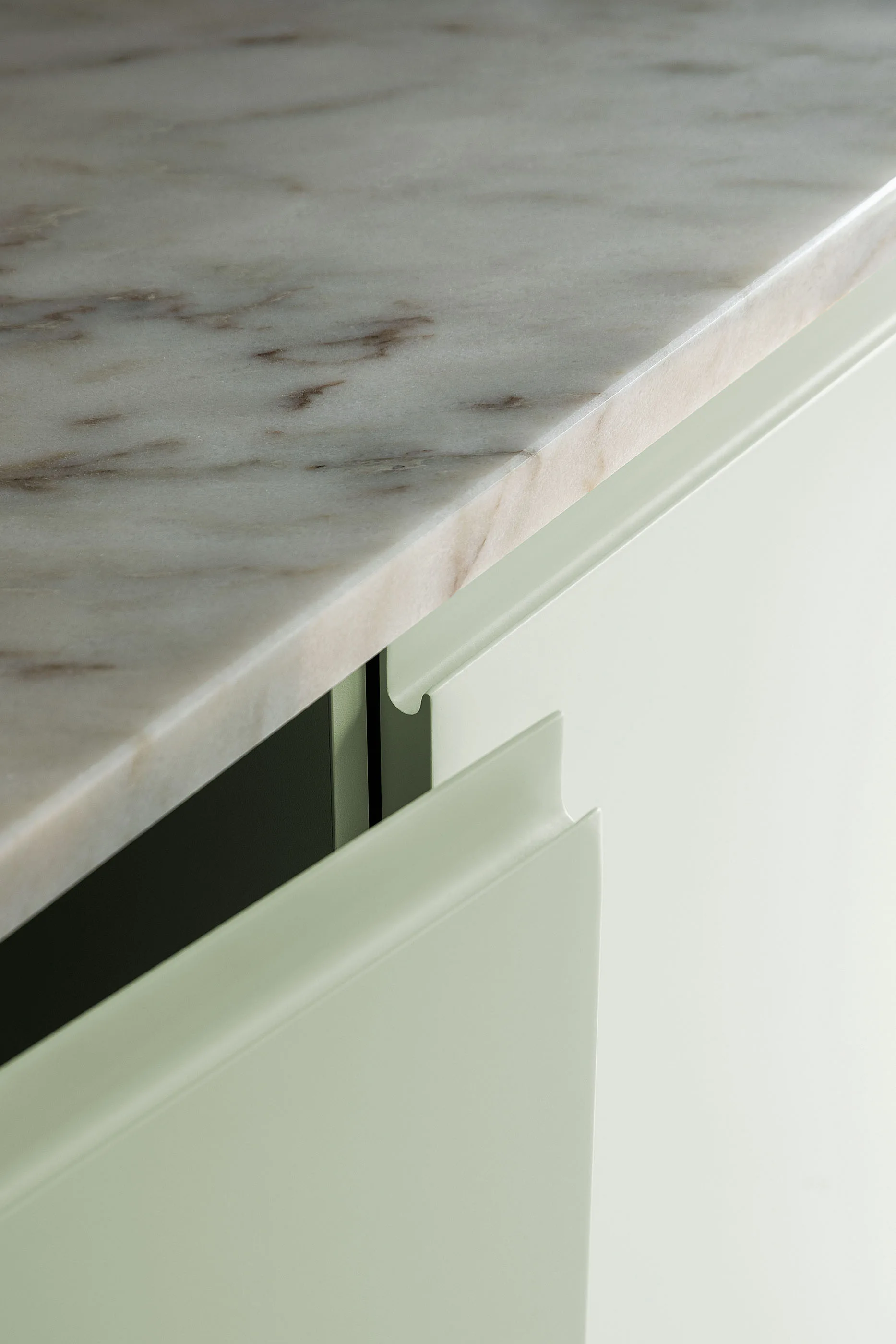 A close-up of a veined white marble countertop resting on pale mint green cabinet doors with sleek integrated handles.