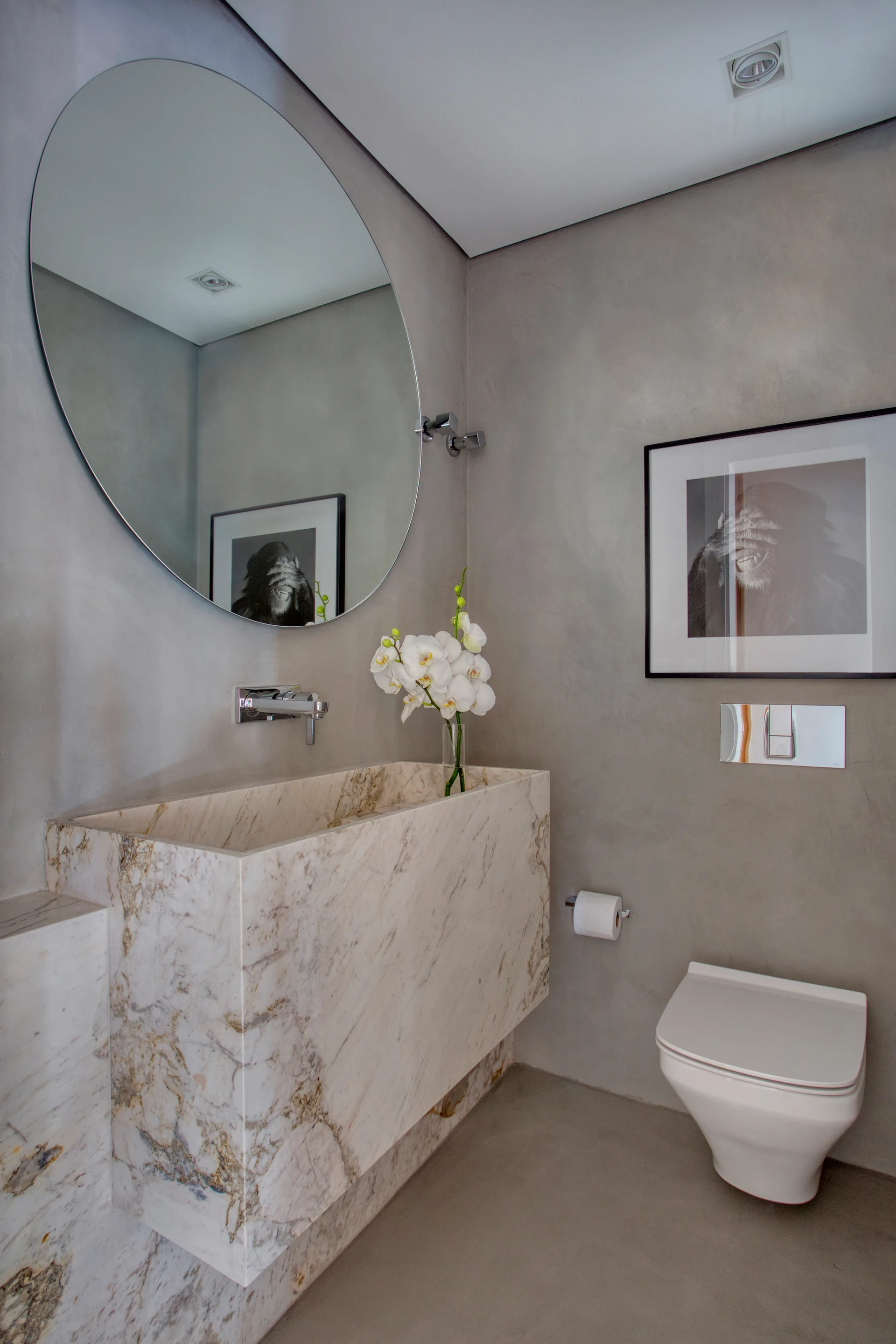 A modern powder room featuring a thick floating marble sink vanity, wall-mounted toilet, circular mirror, and textured grey plaster walls.