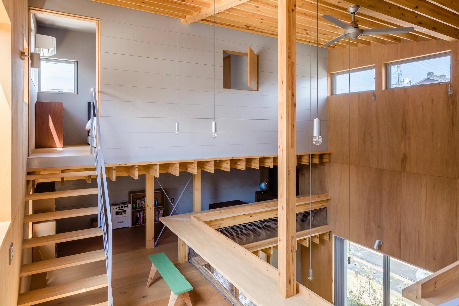A multi-level interior featuring a light wood staircase leading to a loft with grey horizontal plank walls, exposed timber beams, and simple pendant lights.