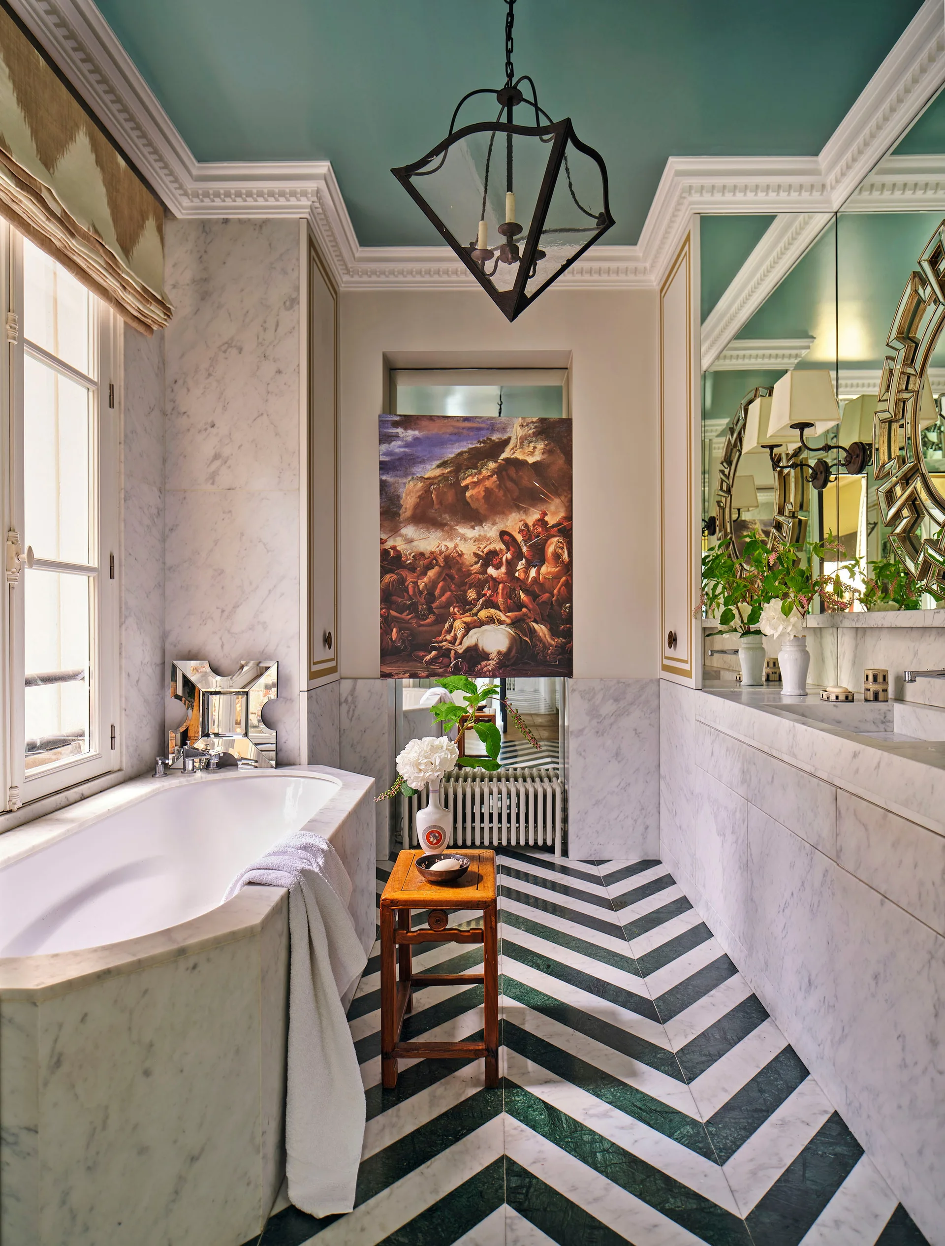 A luxury marble bathroom with a double vanity, a soaking tub, a green-and-white chevron floor, and a bold teal painted ceiling.