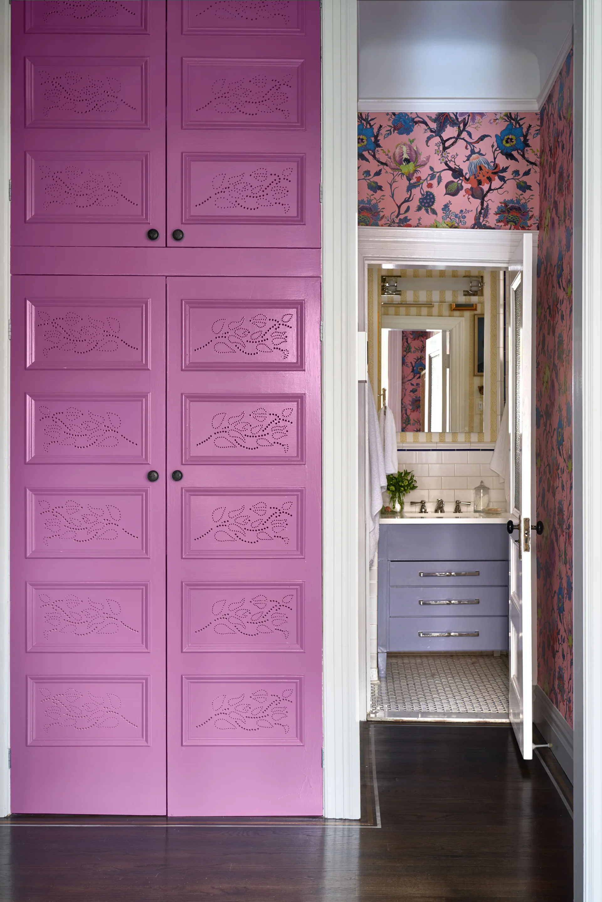 An open doorway reveals a bathroom with pink floral wallpaper and a purple vanity next to a large magenta hallway cabinet with perforated leaf designs.