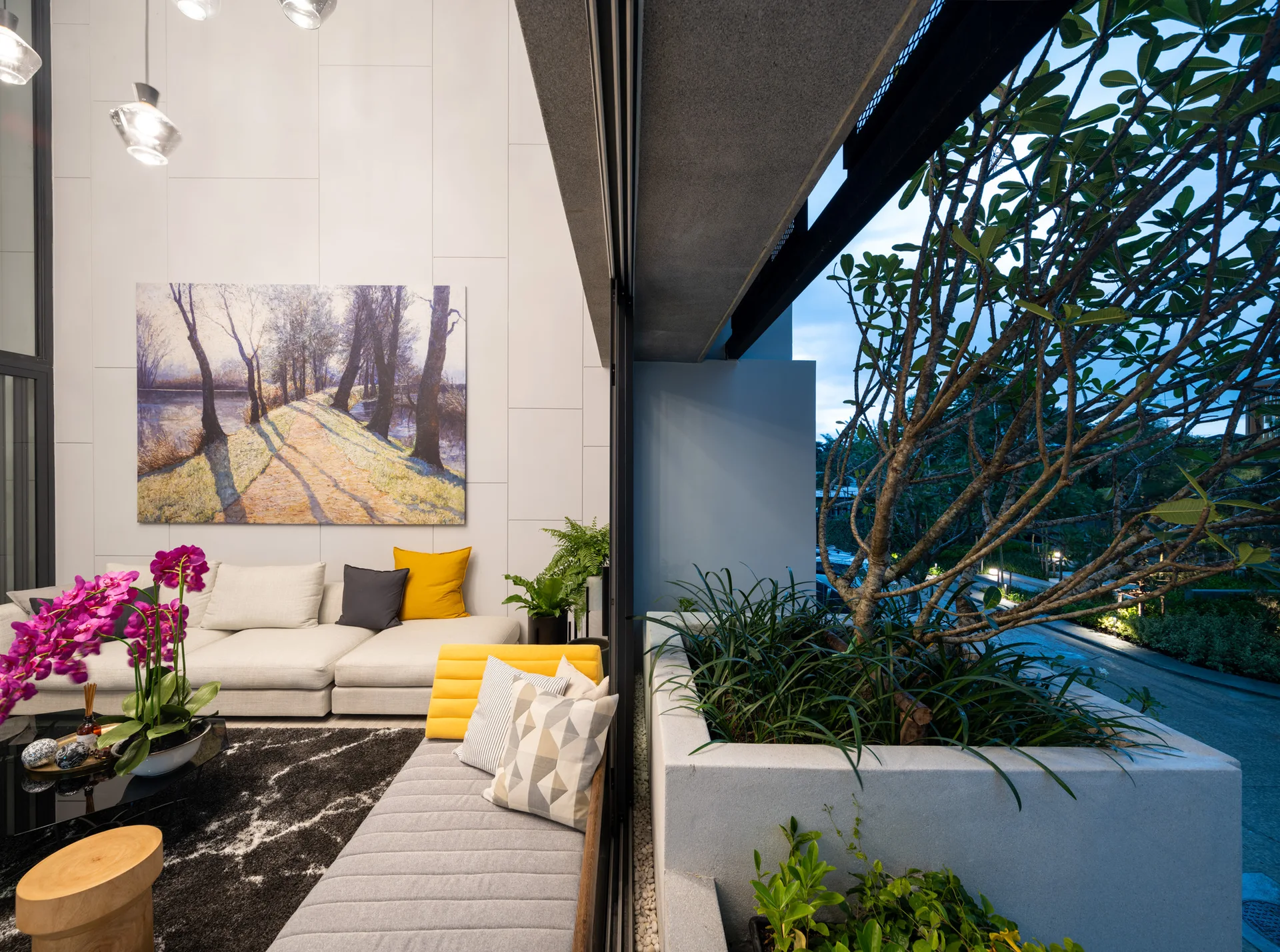A modern cream sectional sofa sits inside a living room next to large sliding glass doors that open to a concrete planter with a green tree.