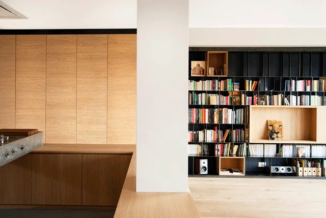 A modern living space featuring a floor-to-ceiling wood cabinet wall alongside a large black metal bookcase divided by a white structural column.