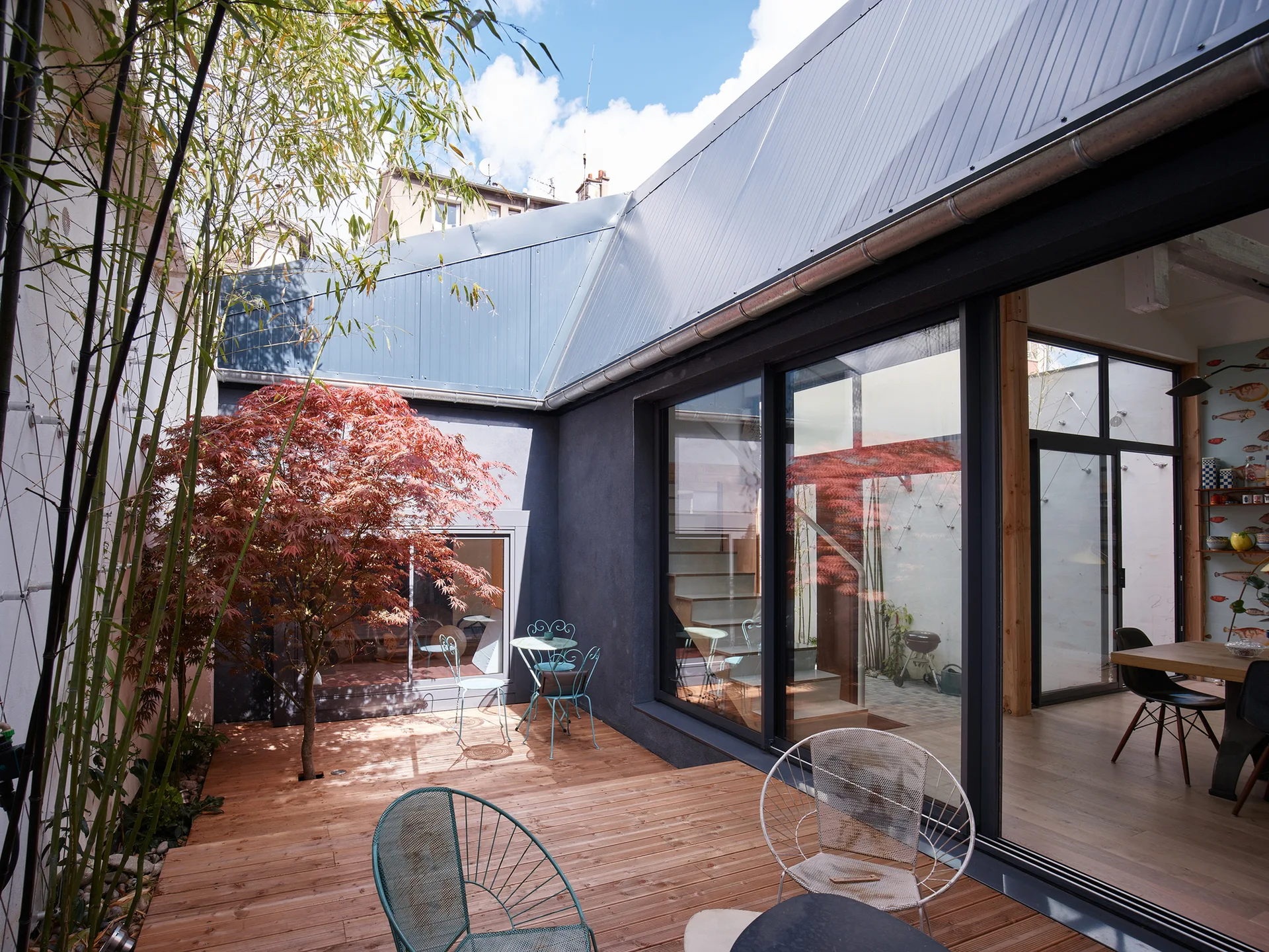 A contemporary courtyard patio features a wooden deck, a red maple tree planted in a cutout, tall bamboo, and sliding glass doors.