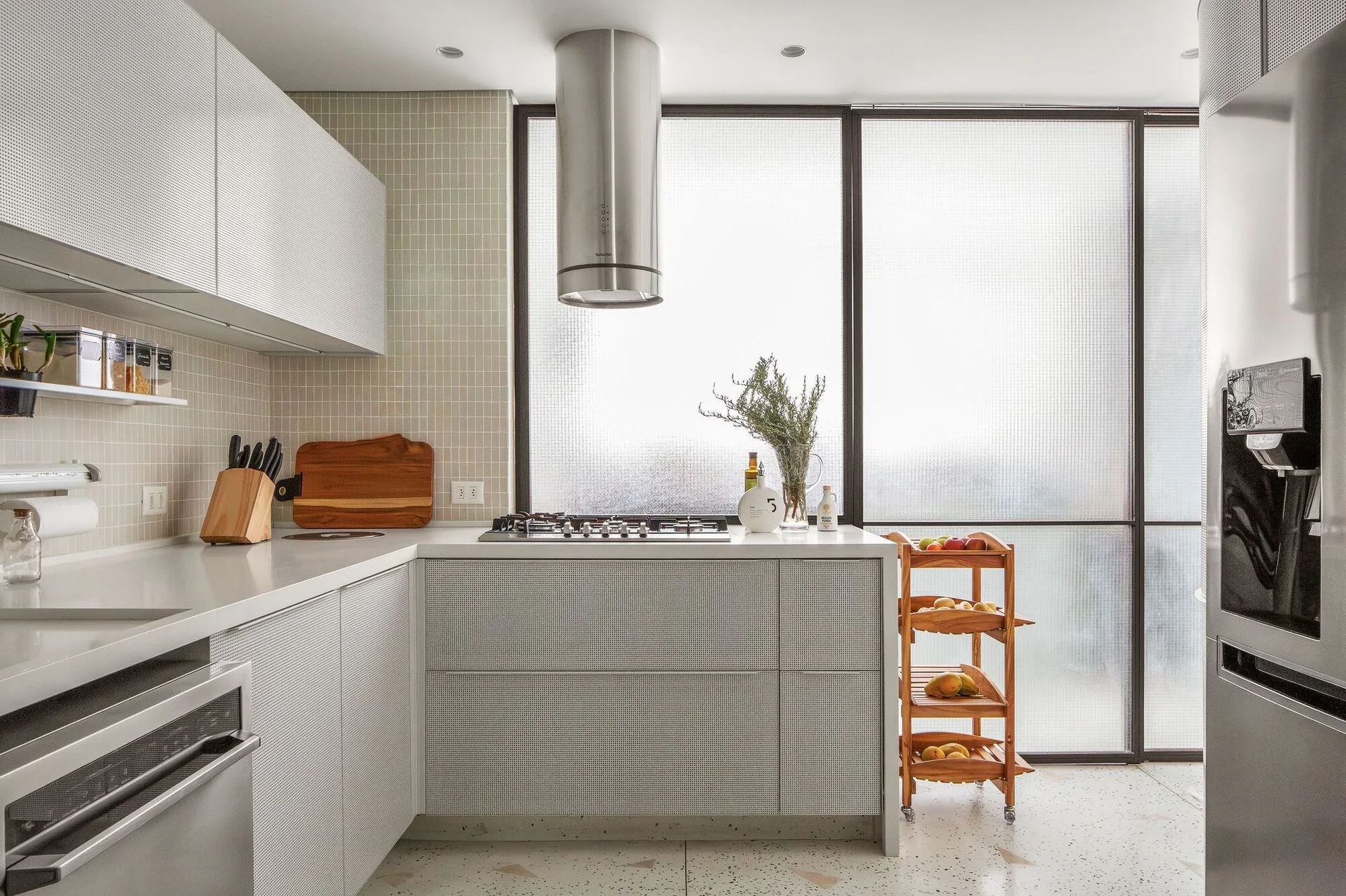 Modern kitchen featuring white perforated cabinets, a cylindrical metal range hood, and a large grid-framed frosted glass window.