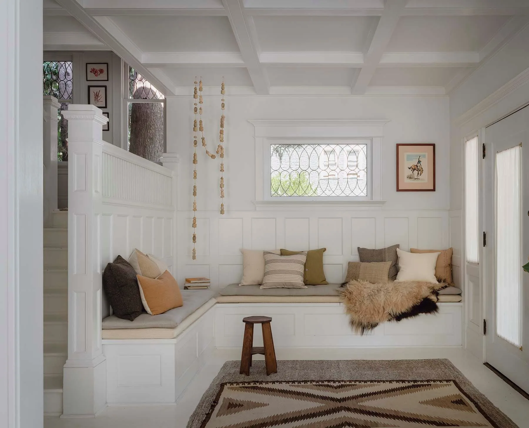 A bright white entryway features an L-shaped built-in bench with pillows, wainscoting on the walls, and a white coffered ceiling.