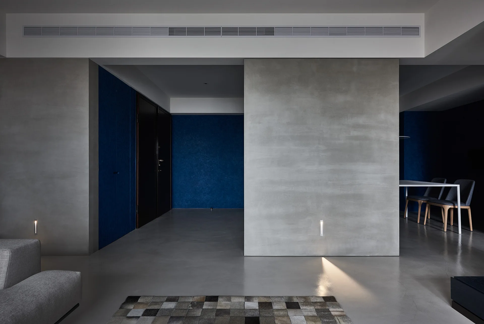 A minimalist interior features smooth concrete partition walls, deep blue accent walls, polished grey floors, and low-level accent lighting.