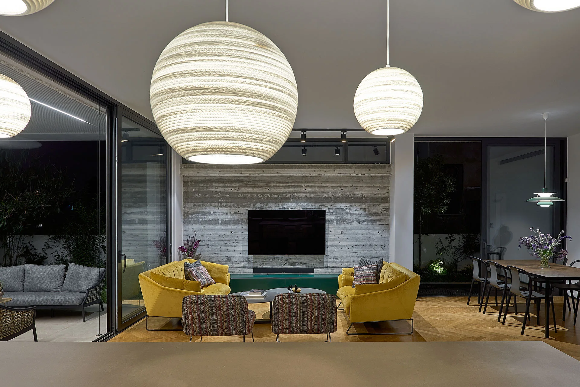 A modern living room with two yellow sofas facing each other beneath large round pendant lights, set against a board-formed concrete wall.