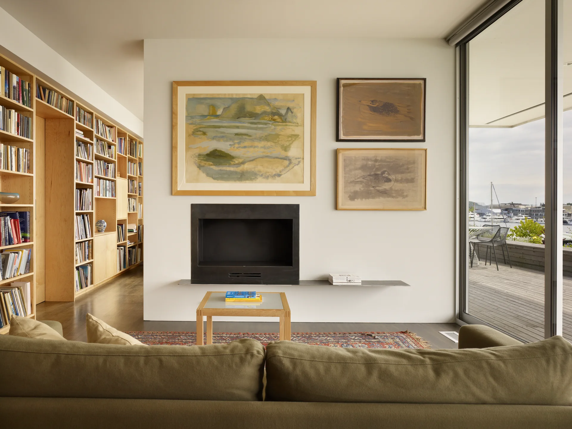 An off-white living room featuring a green sofa, a built-in light wood bookcase, a minimalist black fireplace, and three framed art pieces on the wall.