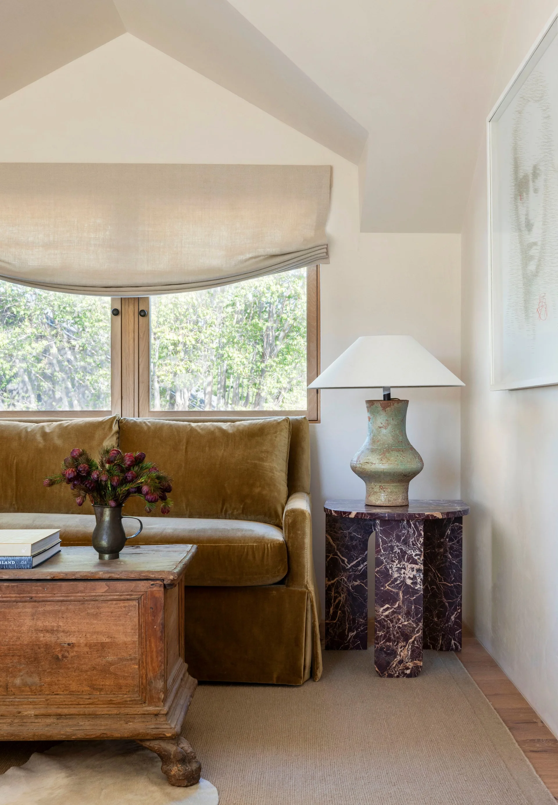 An ochre velvet sofa is paired with a rustic wooden chest coffee table and a dark veined marble side table with a ceramic lamp.