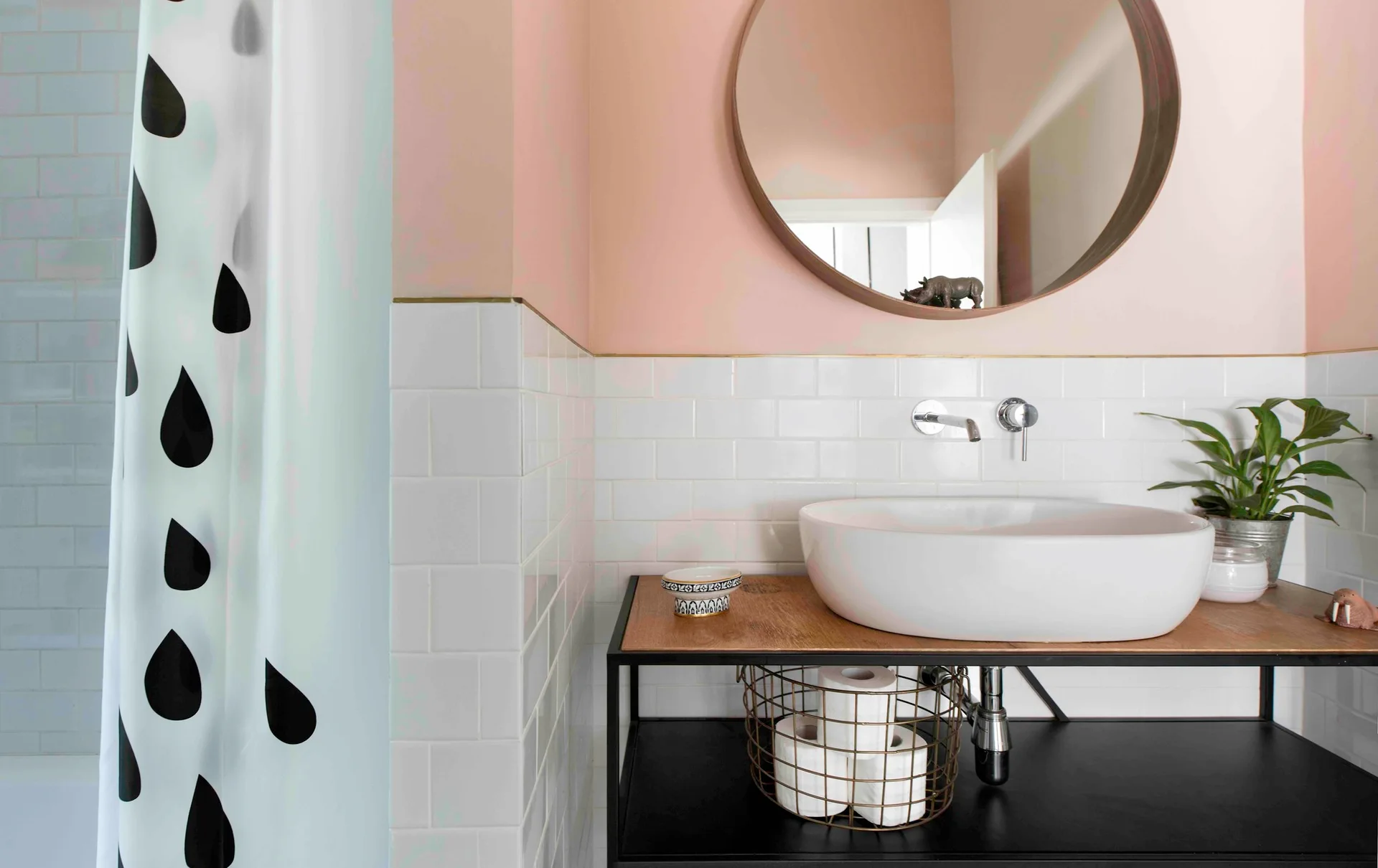 A modern bathroom features a white vessel sink on an open black vanity console against a white subway tile wall with a round mirror.