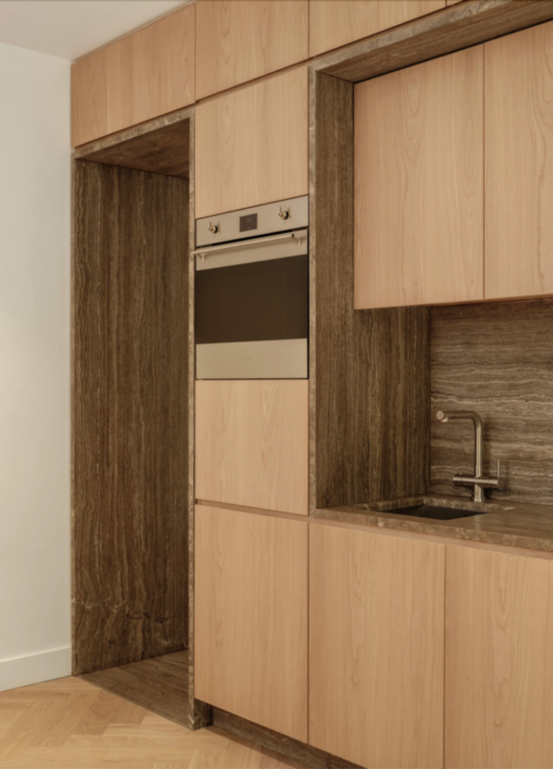 Flat-front wood kitchen cabinets feature built-in appliances and custom stone-lined niches surrounding a sink and a tall alcove.