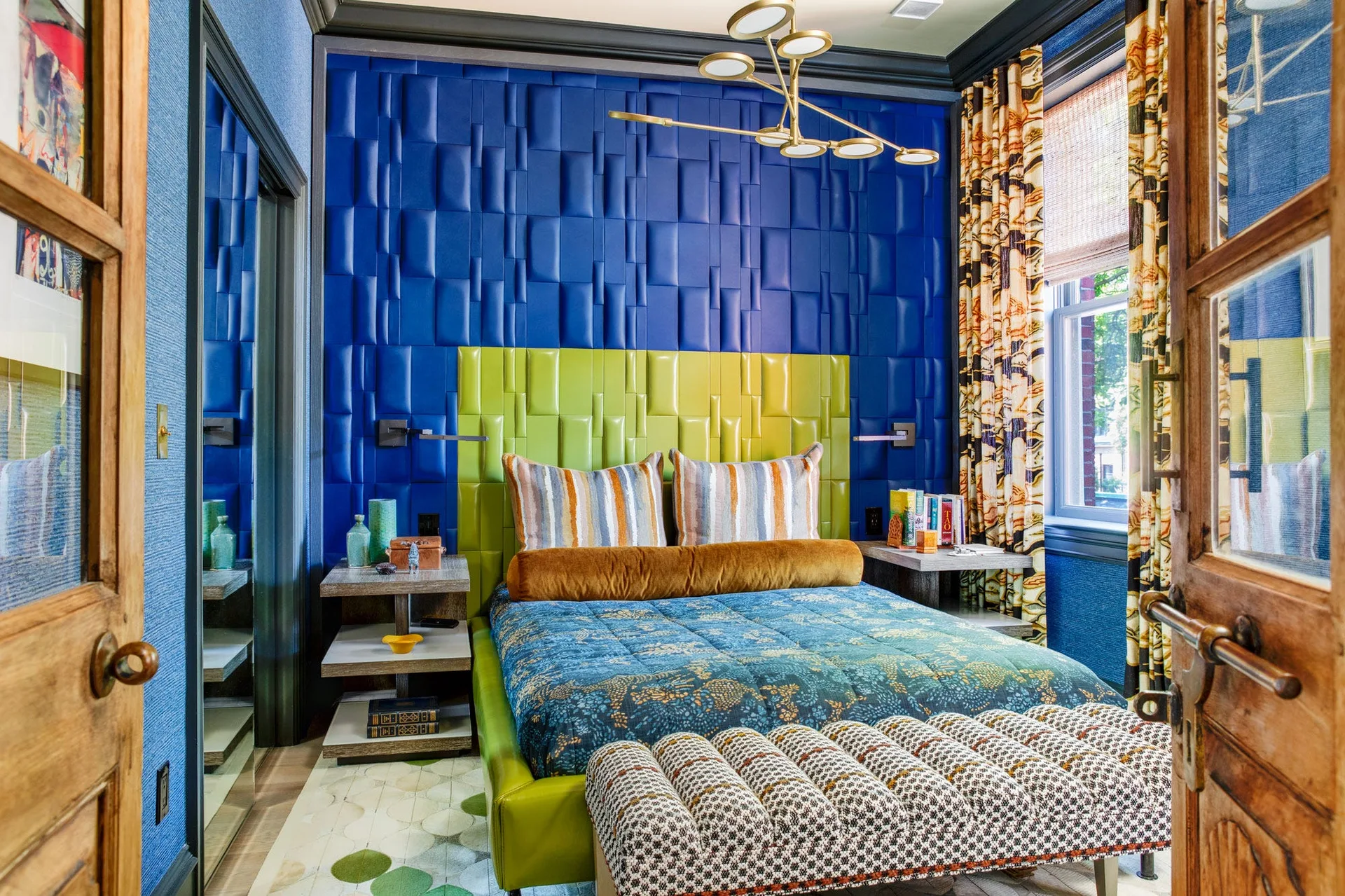 An eclectic bedroom featuring a cobalt blue padded geometric accent wall, a lime green upholstered headboard, and a gold branching chandelier.