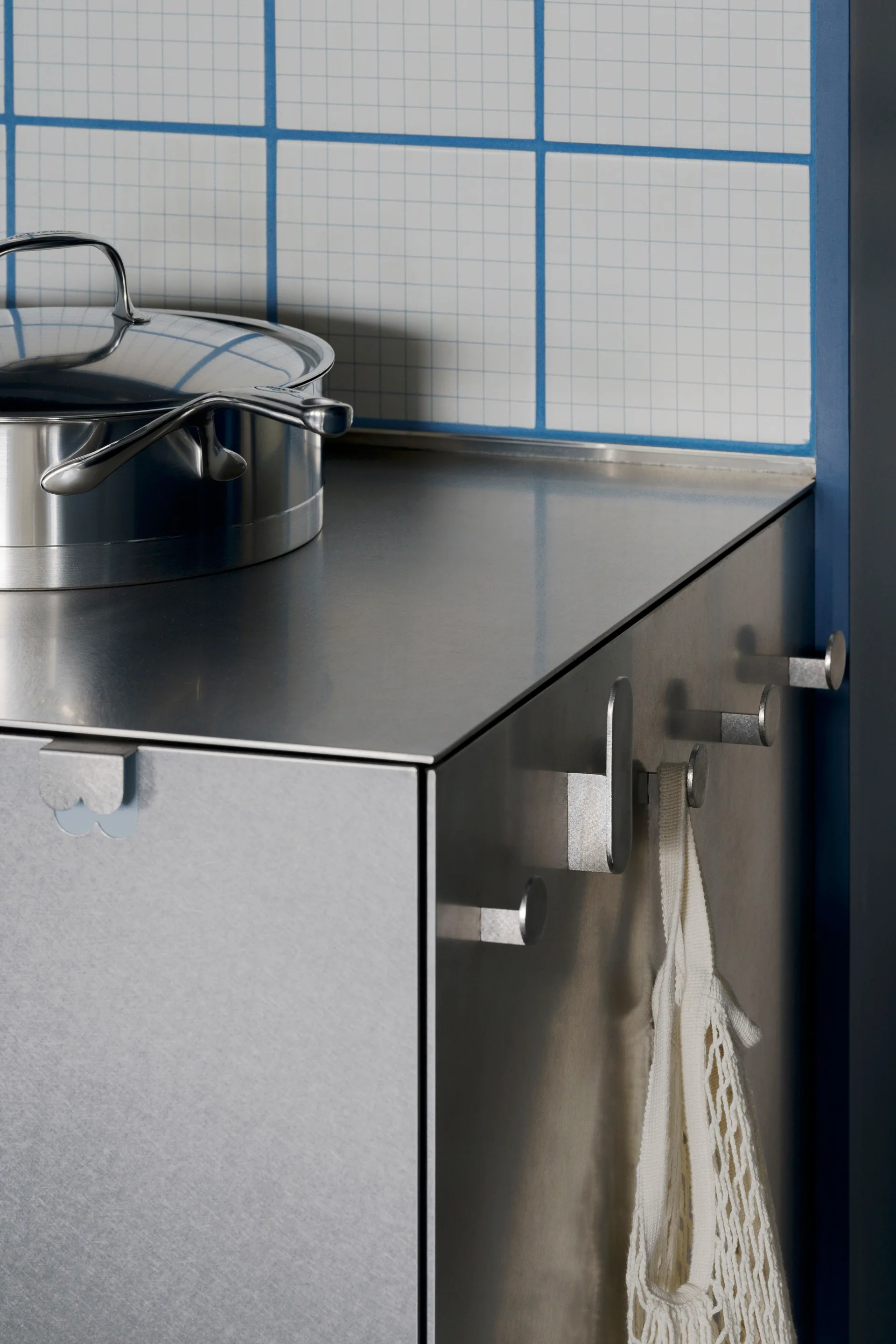 A stainless steel kitchen cabinet with a matching countertop is set against a white tiled backsplash with blue grout lines.