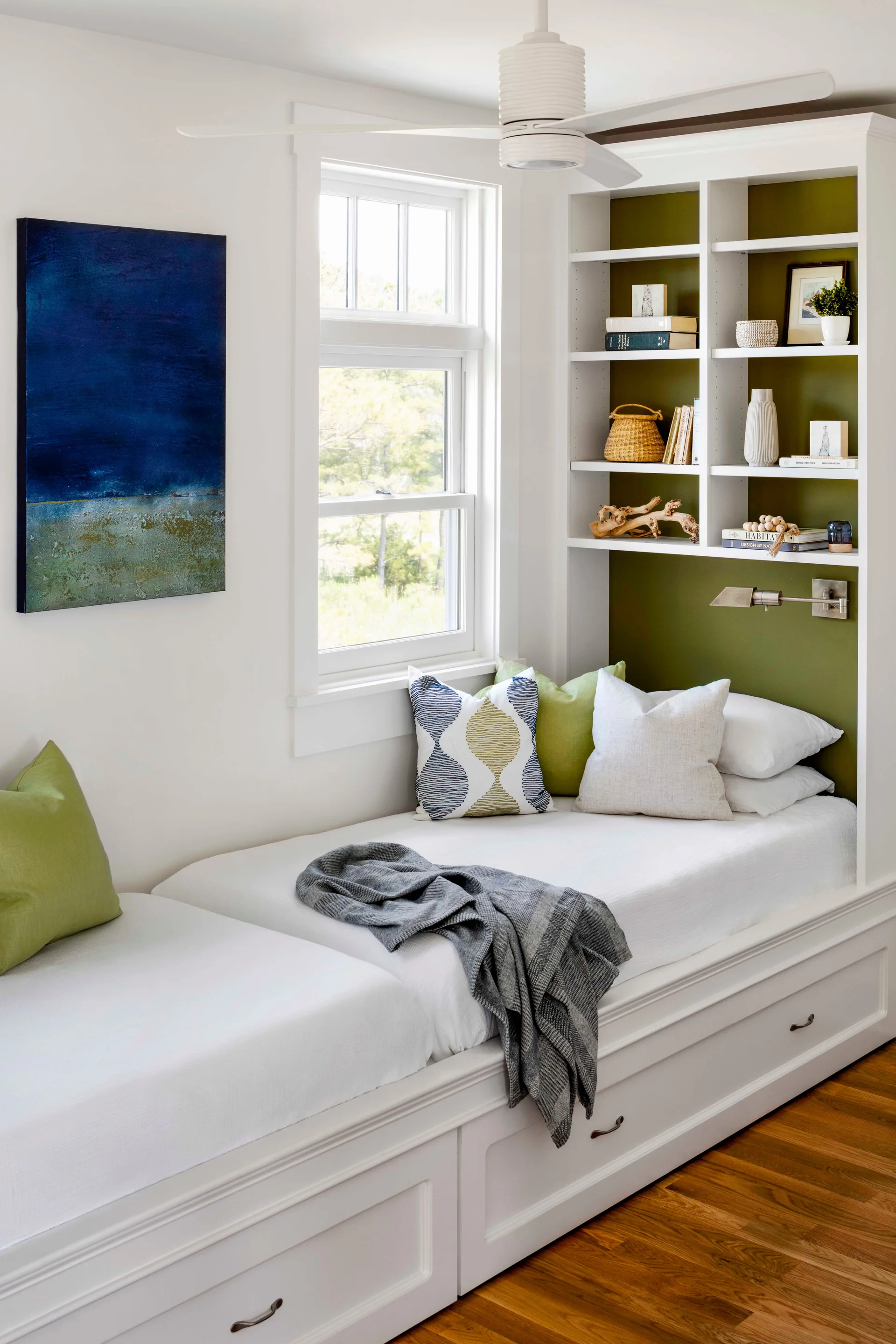 A white built-in daybed with under-bed storage drawers sits next to a window and a bookshelf unit featuring an olive green back wall.