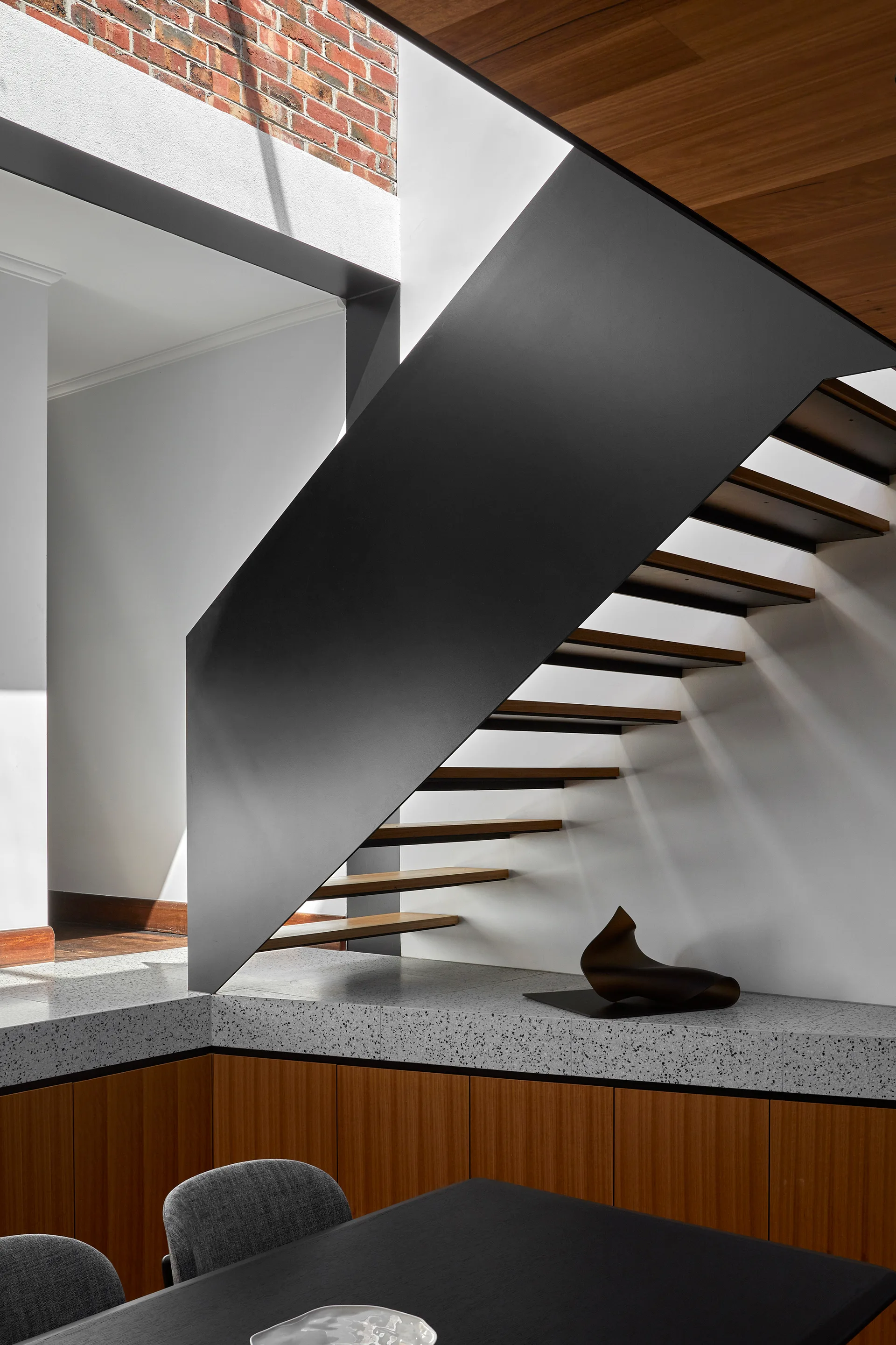 A modern staircase features a solid black metal balustrade, wooden treads, and a speckled grey terrazzo-topped wood cabinet base.