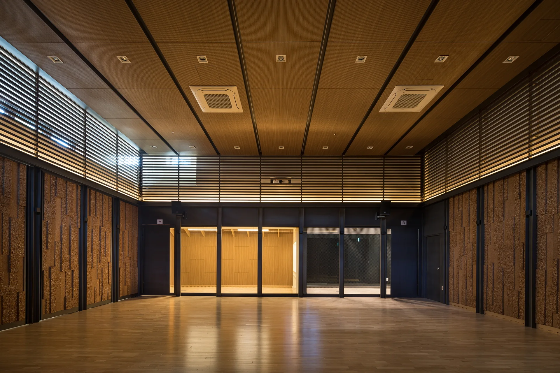 A large empty room featuring textured wood wall panels, horizontal slatted wood screens, a wood plank ceiling, and polished floors.