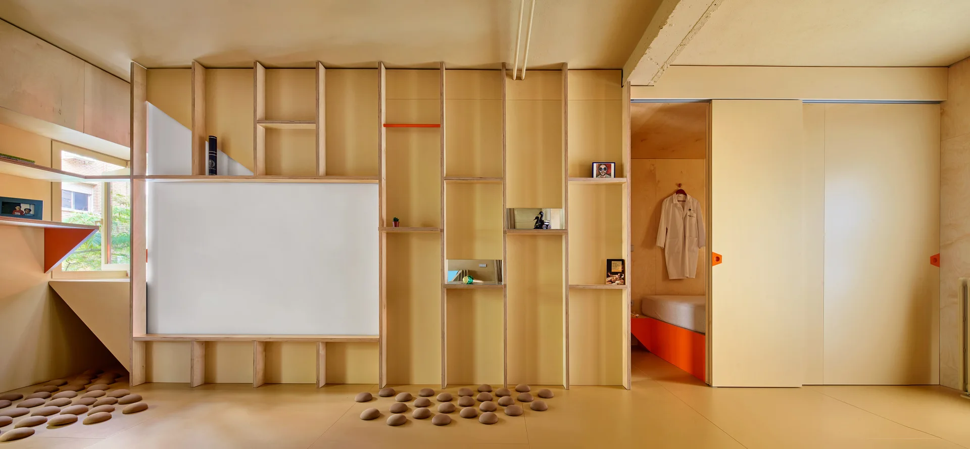 A yellow room featuring a custom plywood partition wall with built-in open shelves, a sliding door, and a view into a small bedroom niche.