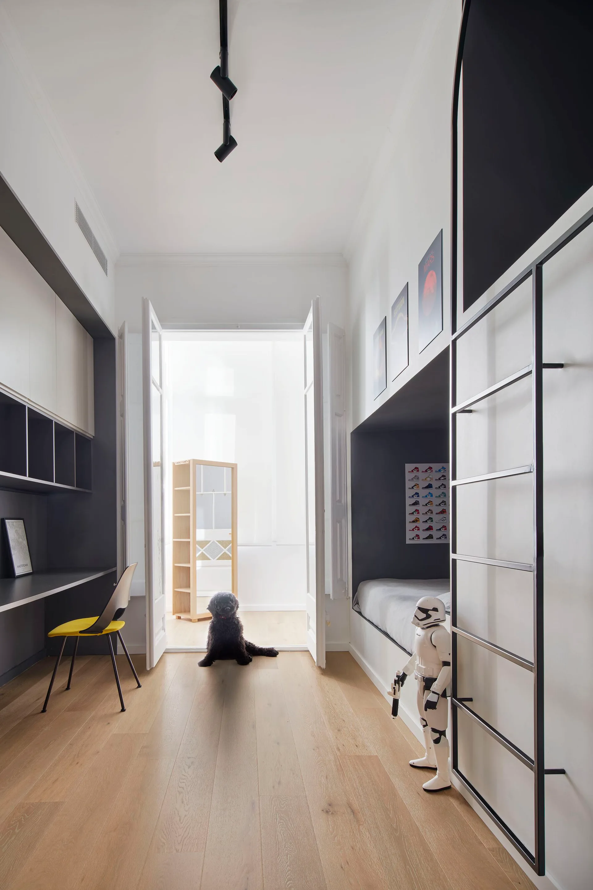 A modern minimalist kids bedroom with integrated black bunk beds, a built-in grey study desk, and light wood flooring.